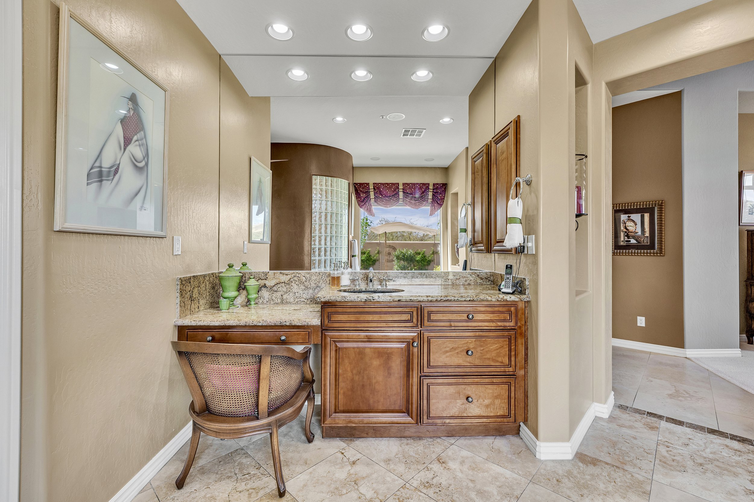 This Scottsdale, AZ bathroom vanity area features a wooden cabinet, granite countertop, and a cozy seating area, captured with professional real estate photography to highlight its elegant design.