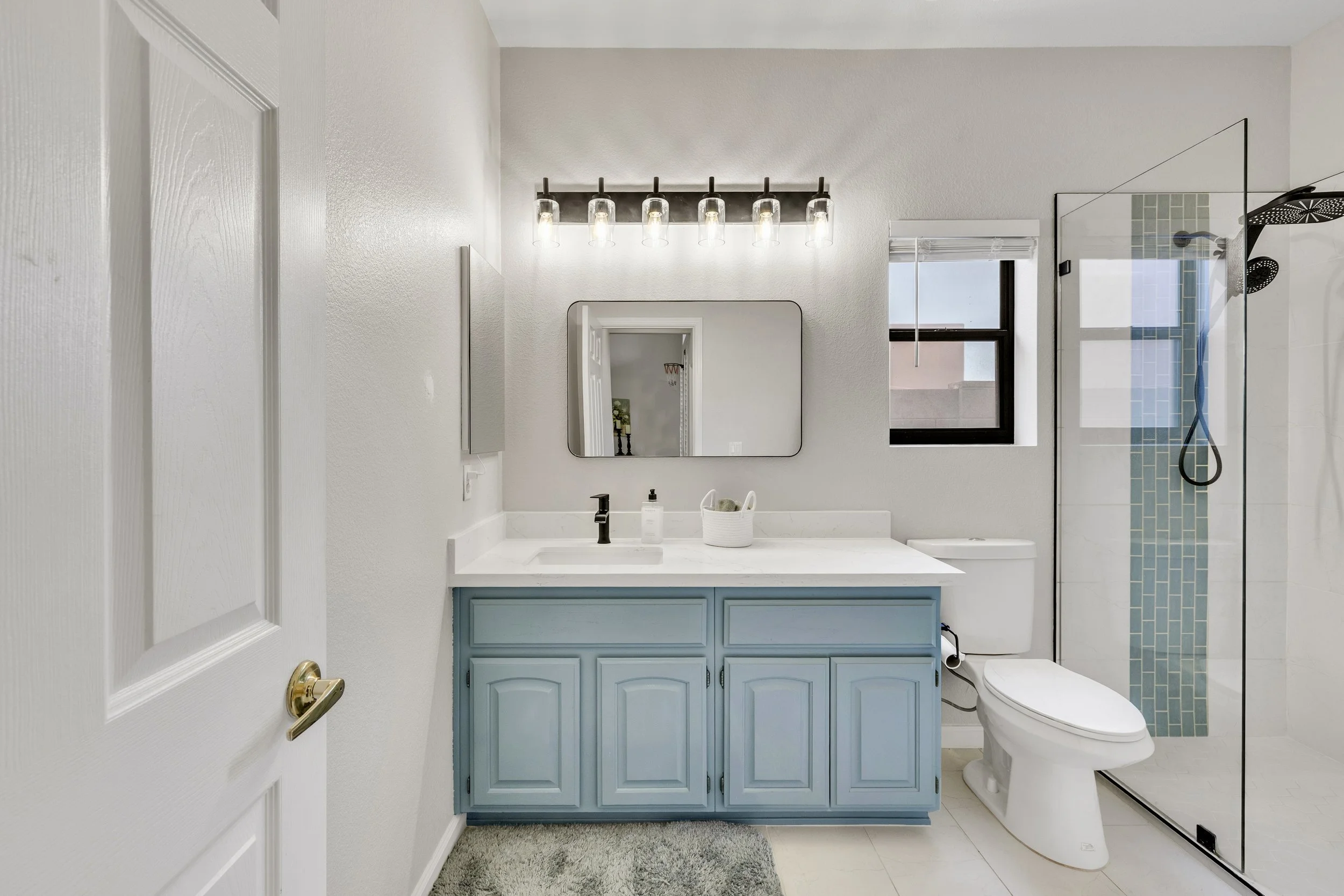 This bathroom in Goodyear, AZ features a blue vanity, glass shower enclosure, and modern fixtures, captured perfectly through professional real estate photography.