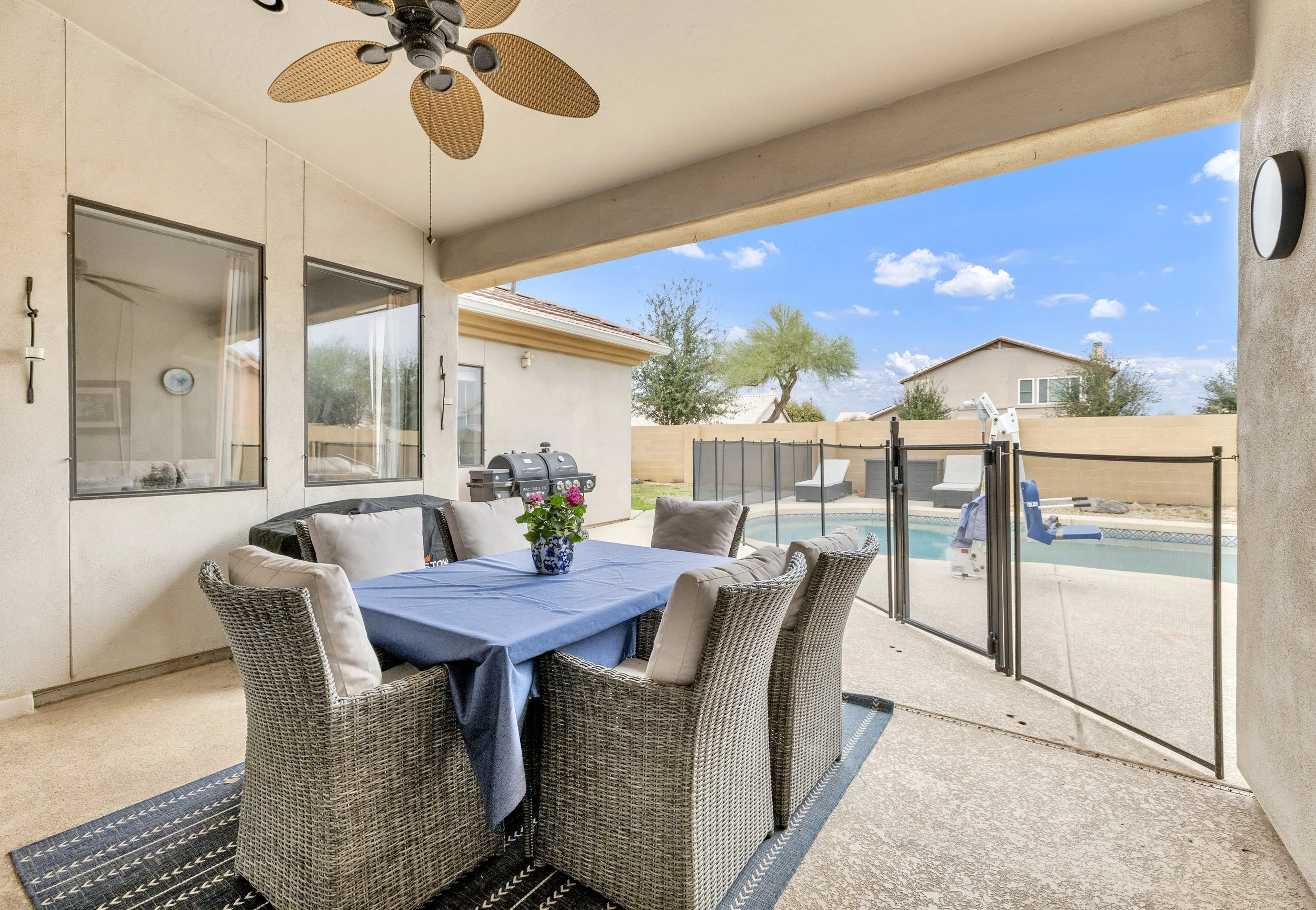 This covered patio dining area overlooks a fenced swimming pool, offering a comfortable outdoor space in Goodyear, AZ, captured with expert real estate photography.
