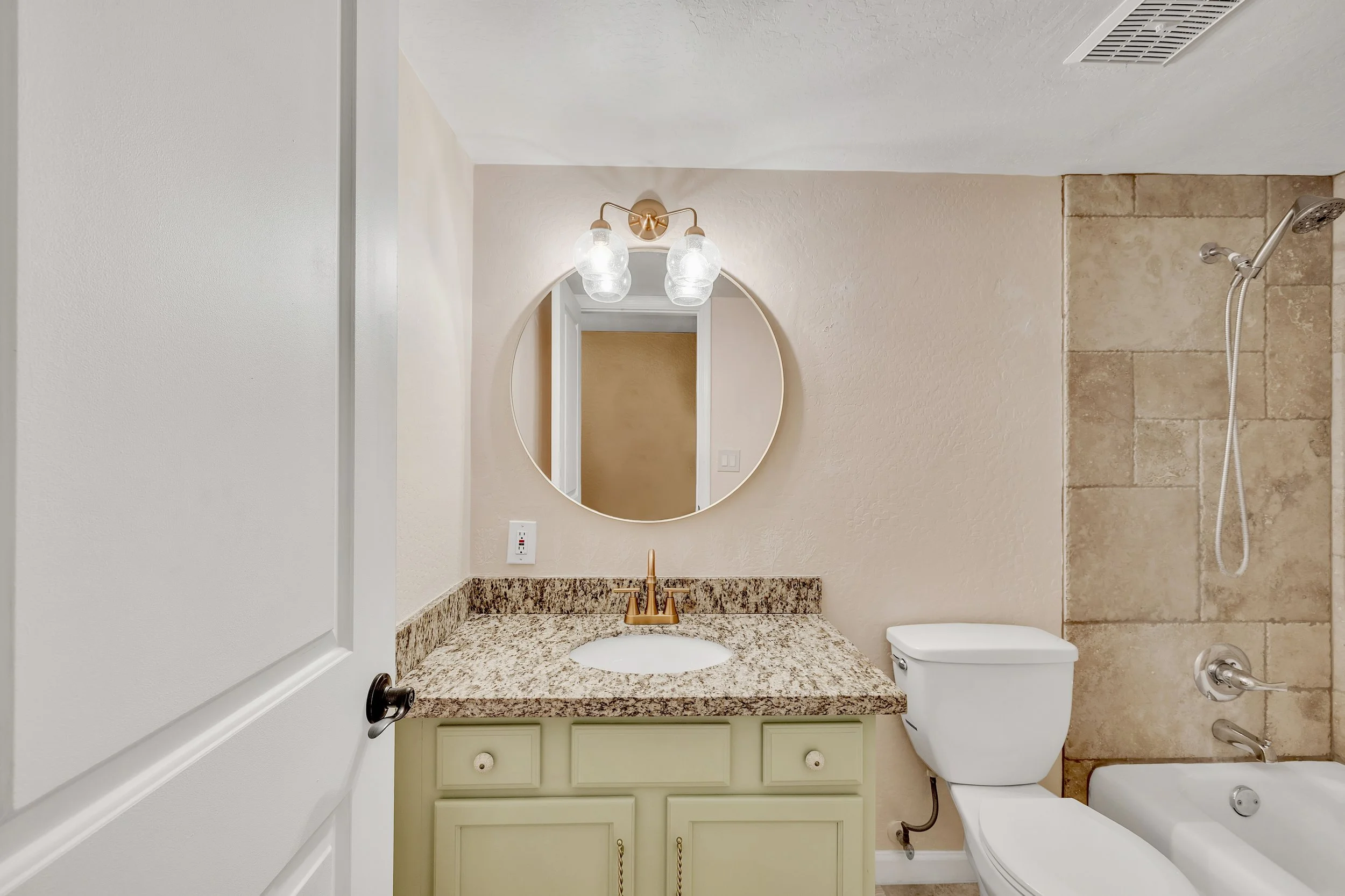 This bright bathroom features a modern vanity with granite countertop and a round mirror, showcasing clean design in Tempe, AZ, captured with professional real estate photography.