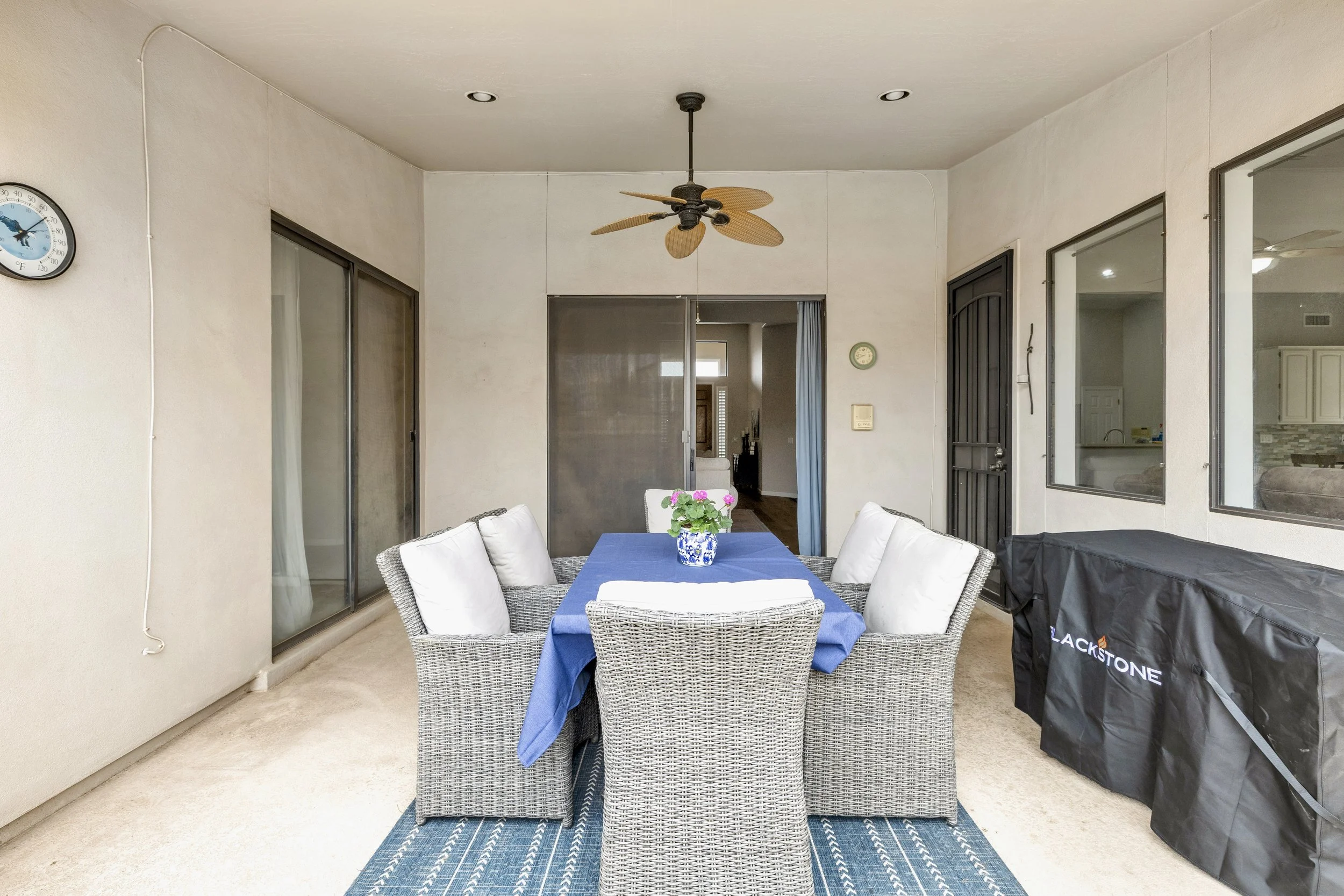 This covered patio dining area in Goodyear, AZ features comfortable wicker furniture and a ceiling fan, perfect for outdoor gatherings, showcased through professional real estate photography.