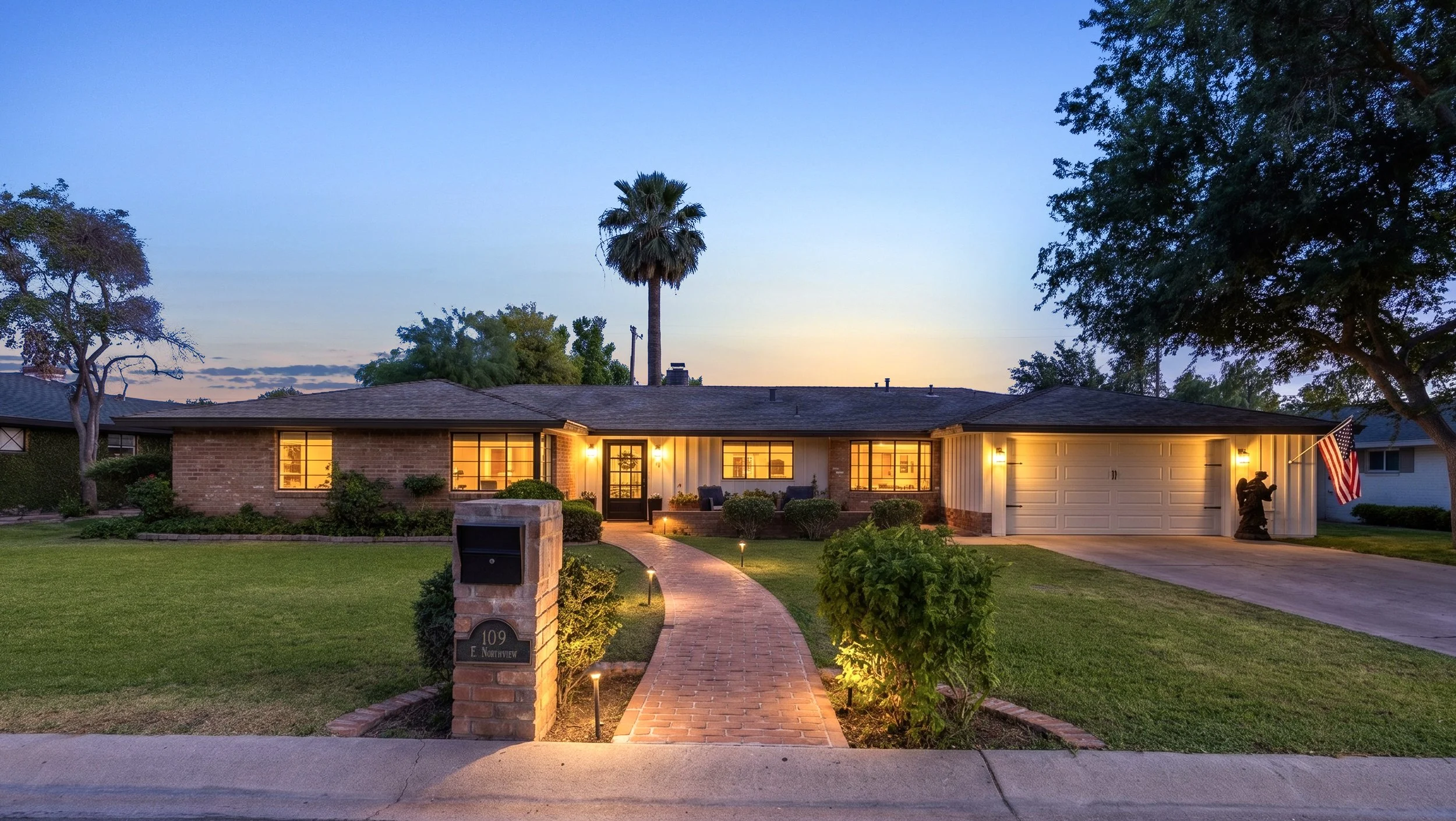 This twilight real estate photography showcases a charming brick home with an inviting lit pathway and garage in Phoenix, AZ, highlighting its warm and welcoming exterior ambiance.