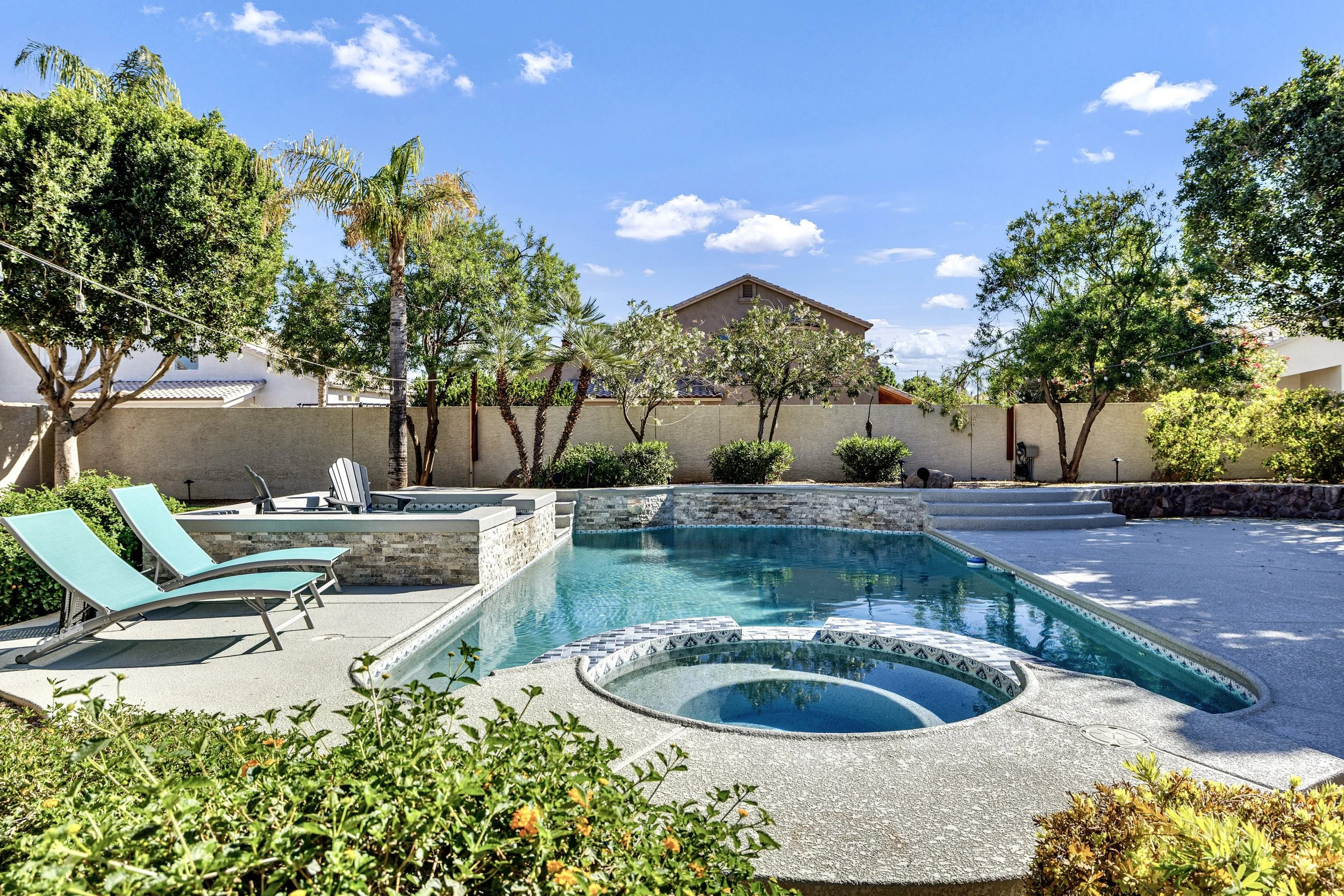 This Gilbert, AZ backyard features a sparkling pool, attached spa, and lush landscaping, captured with expert real estate photography to highlight its inviting outdoor living space.