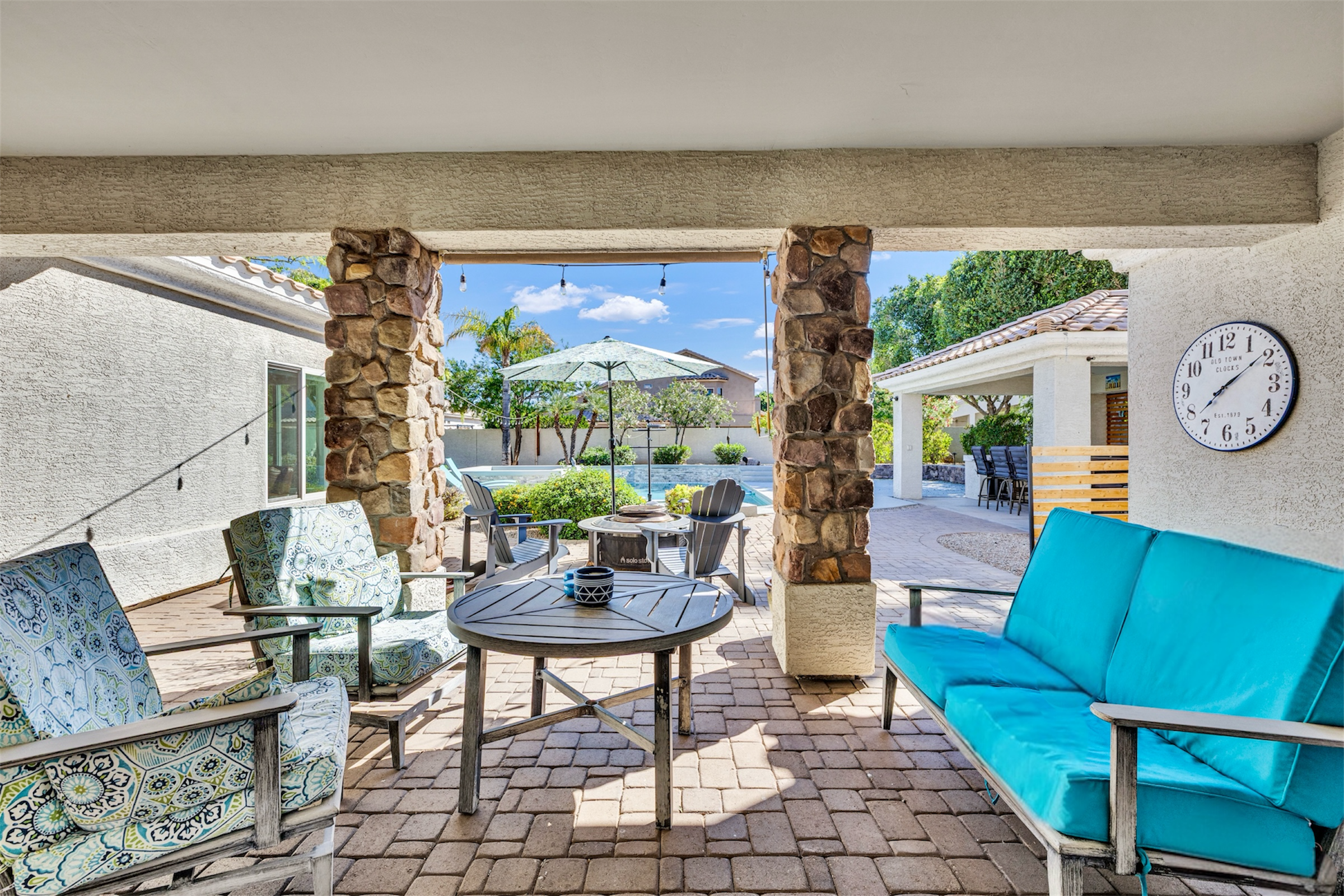 This Gilbert, AZ home features a covered patio with stone pillars, scenic pool views, and comfortable outdoor seating, perfectly showcased through professional real estate photography.