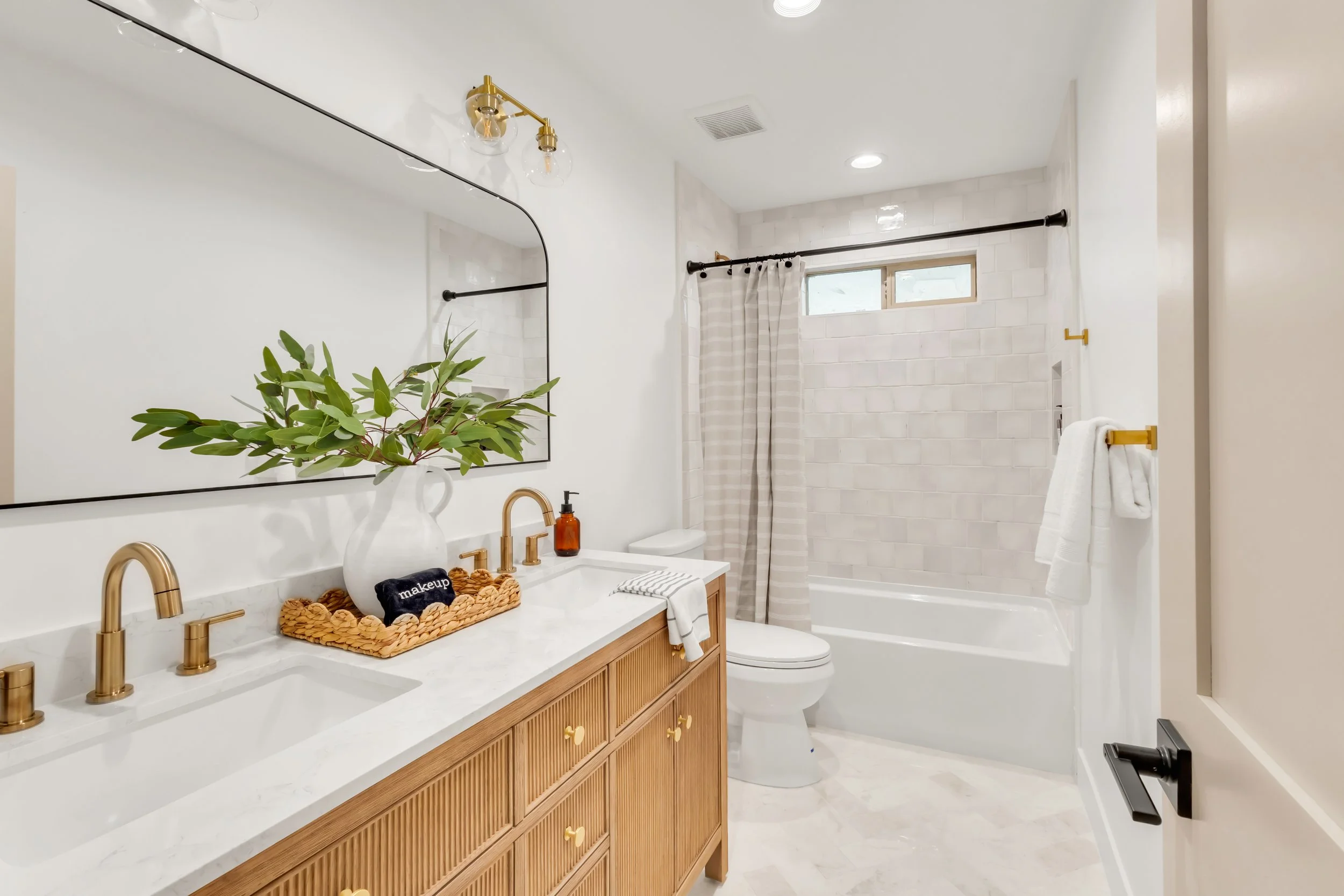 Elegant bathroom in Phoenix, AZ with wood vanity, gold fixtures, and white tile tub surround.