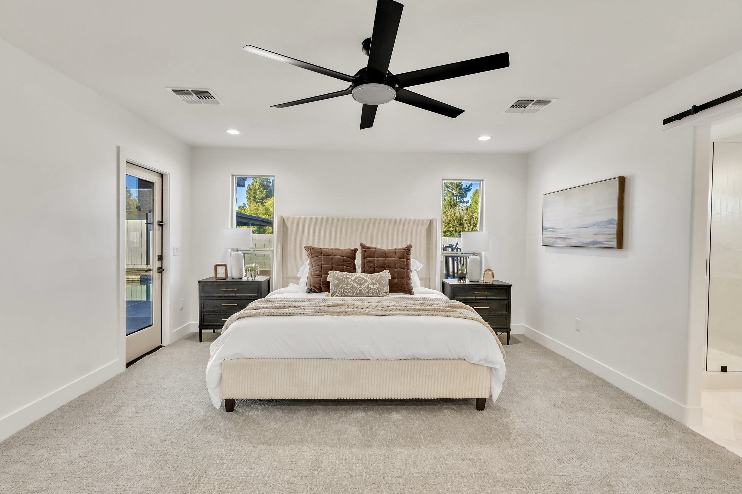 Bright primary bedroom in Phoenix, AZ with black ceiling fan, modern decor, and access to backyard pool area.