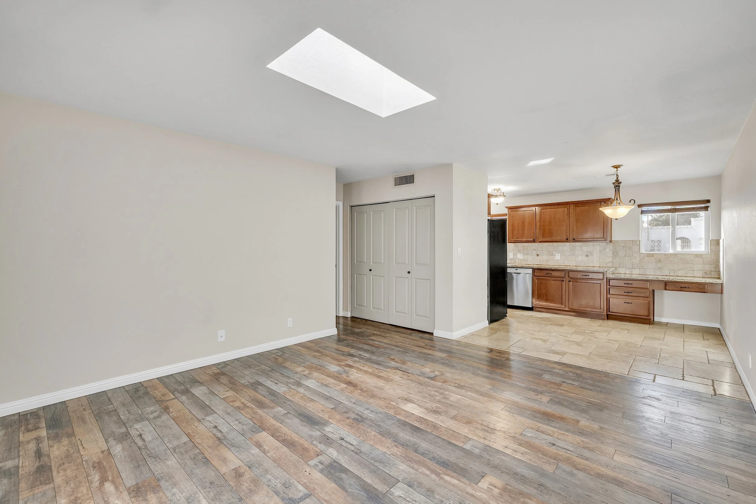 This bright, empty living room with a skylight and kitchen showcases clean finishes and versatility in Tempe, AZ, perfect for real estate photography to highlight modern home features.