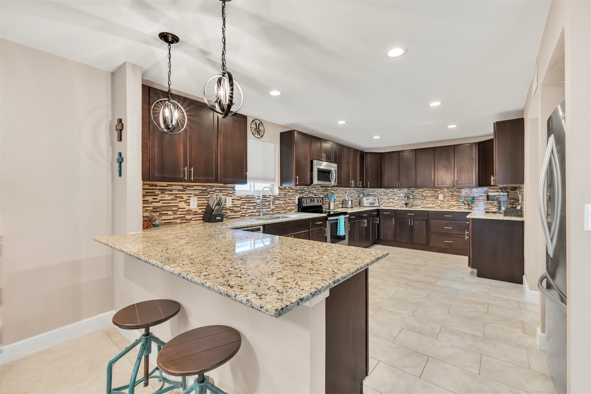 This modern kitchen in Sun Lakes, AZ features granite countertops, dark cabinetry, and stylish pendant lighting, captured expertly with real estate photography to highlight its spacious design.