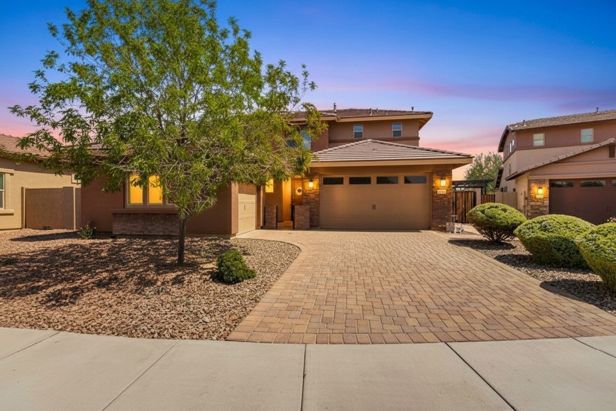 This twilight real estate photography showcases a beautiful two-story house with a driveway, desert landscaping, and glowing window lights in Phoenix, AZ, highlighting its curb appeal and inviting atmosphere.