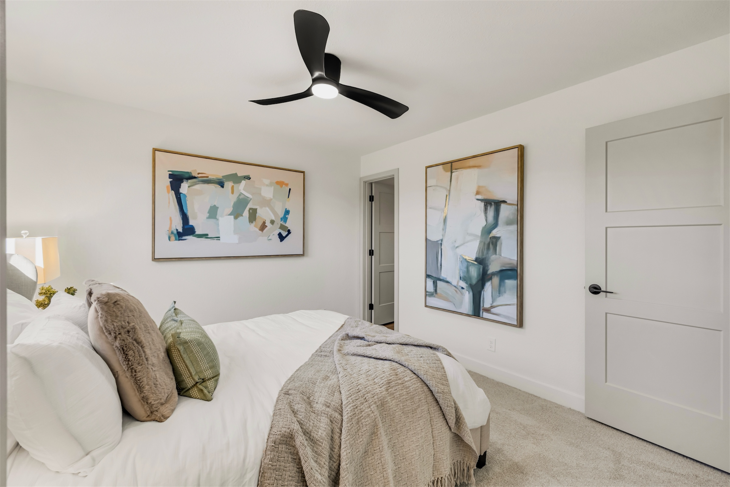 This bright bedroom in Mesa, AZ features modern ceiling fan, abstract artwork, and cozy bedding, captured with expert real estate photography to showcase its inviting design.