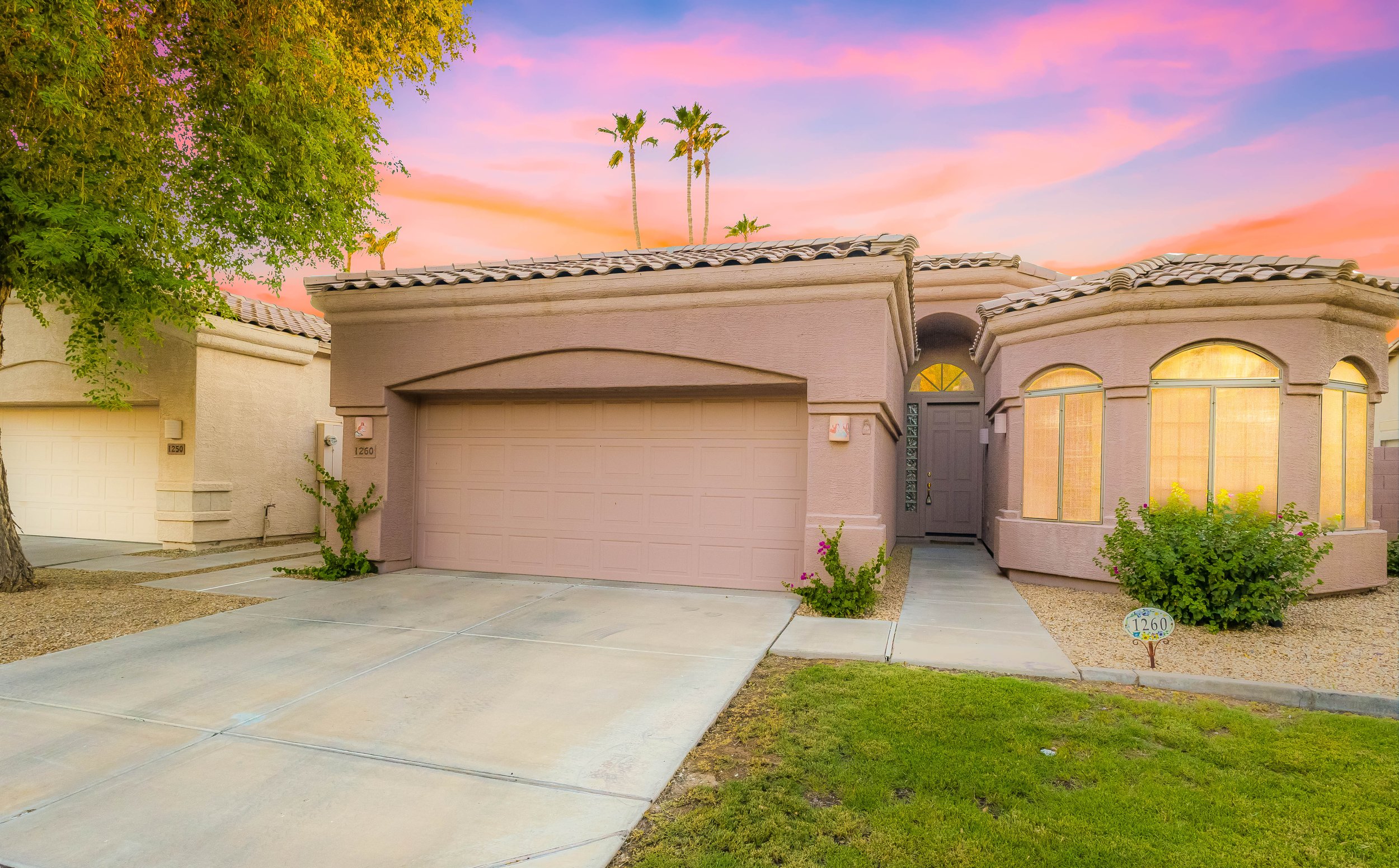 Twilight real estate photography showcases a charming Phoenix, AZ home with warm interior lighting and a well-maintained front yard under a vibrant sunset sky.