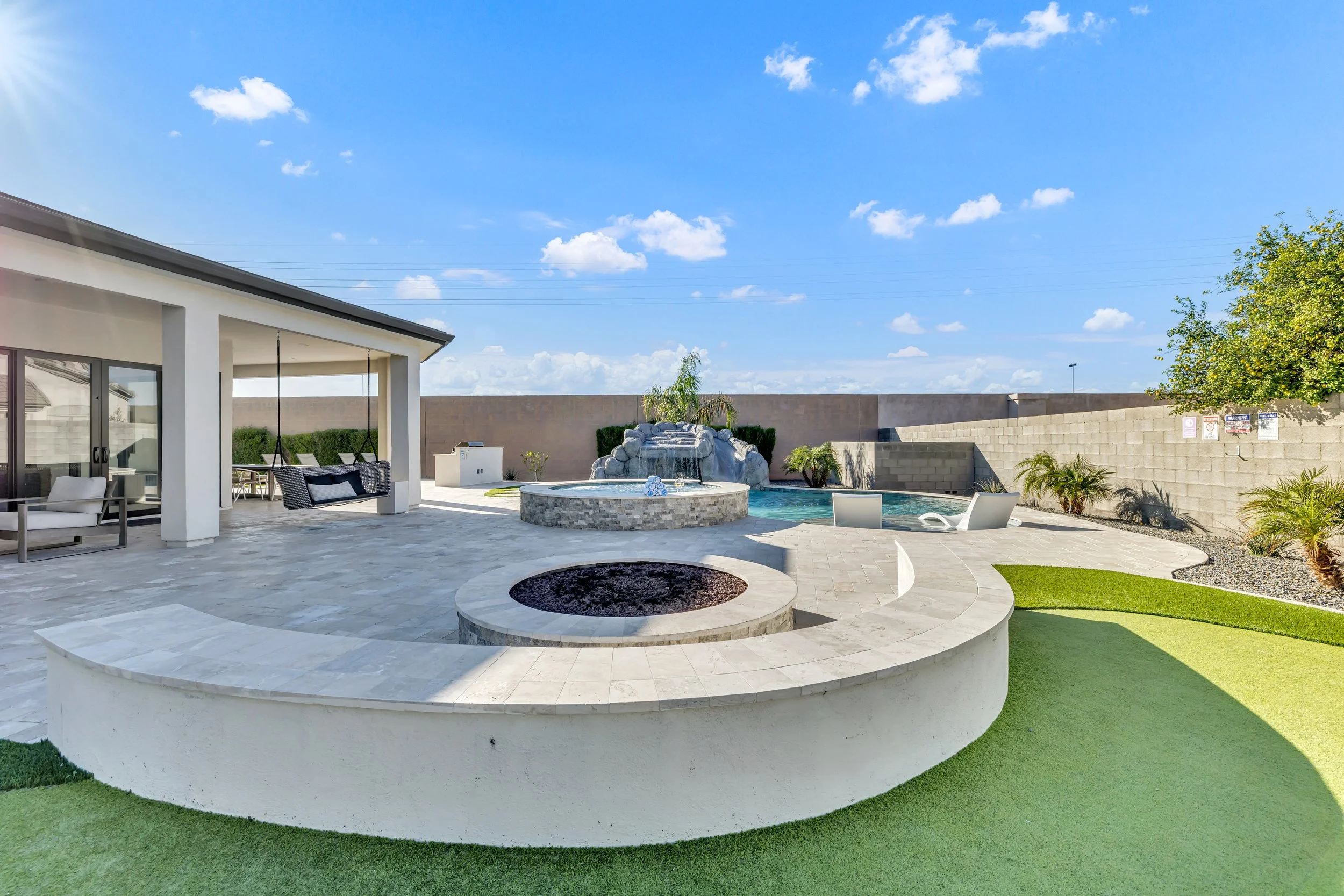 Circular fire pit lounge and tiered patio with stone pavers overlooking pool and waterfall in Scottsdale, Arizona.