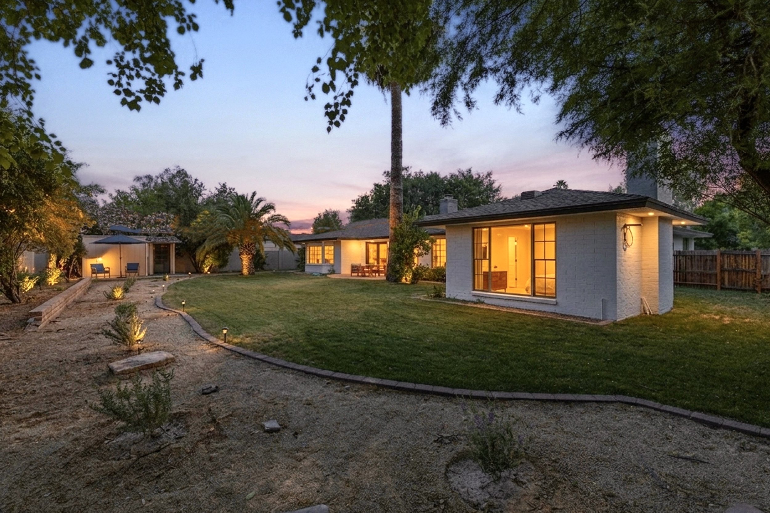 This twilight exterior photo showcases a spacious backyard in Phoenix, AZ, captured with expert real estate photography highlighting the well-lit home and lush green lawn.