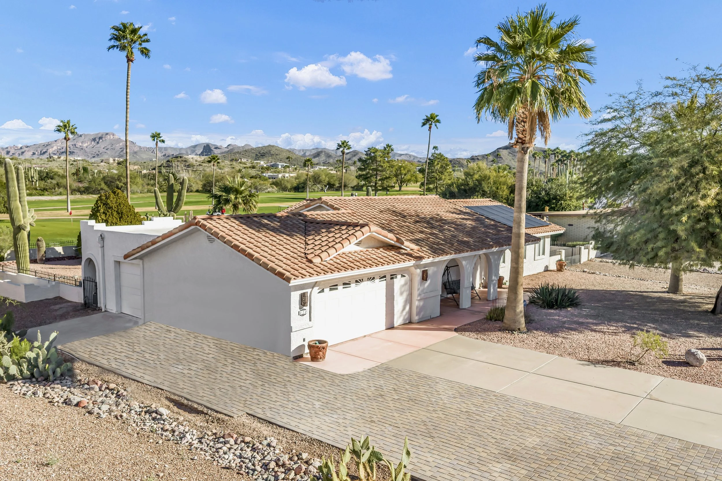 Aerial drone view of a single-story Arizona home with tile roof, desert landscaping, and golf course backdrop.