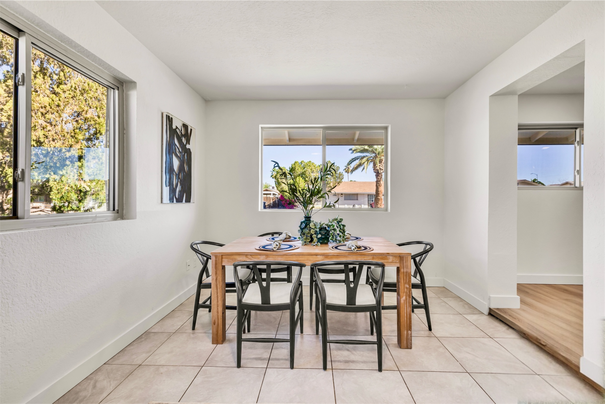 This bright dining room in Mesa, AZ features a wooden table with six black chairs and large windows, captured with professional real estate photography to highlight natural light and modern design.