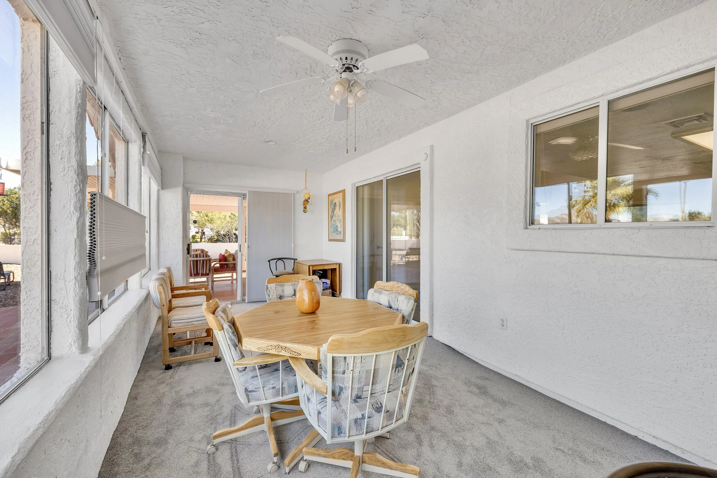 This bright sunroom dining area in Queen Valley, AZ, showcases spacious comfort and natural light, perfect for real estate photography highlighting cozy indoor-outdoor living spaces.