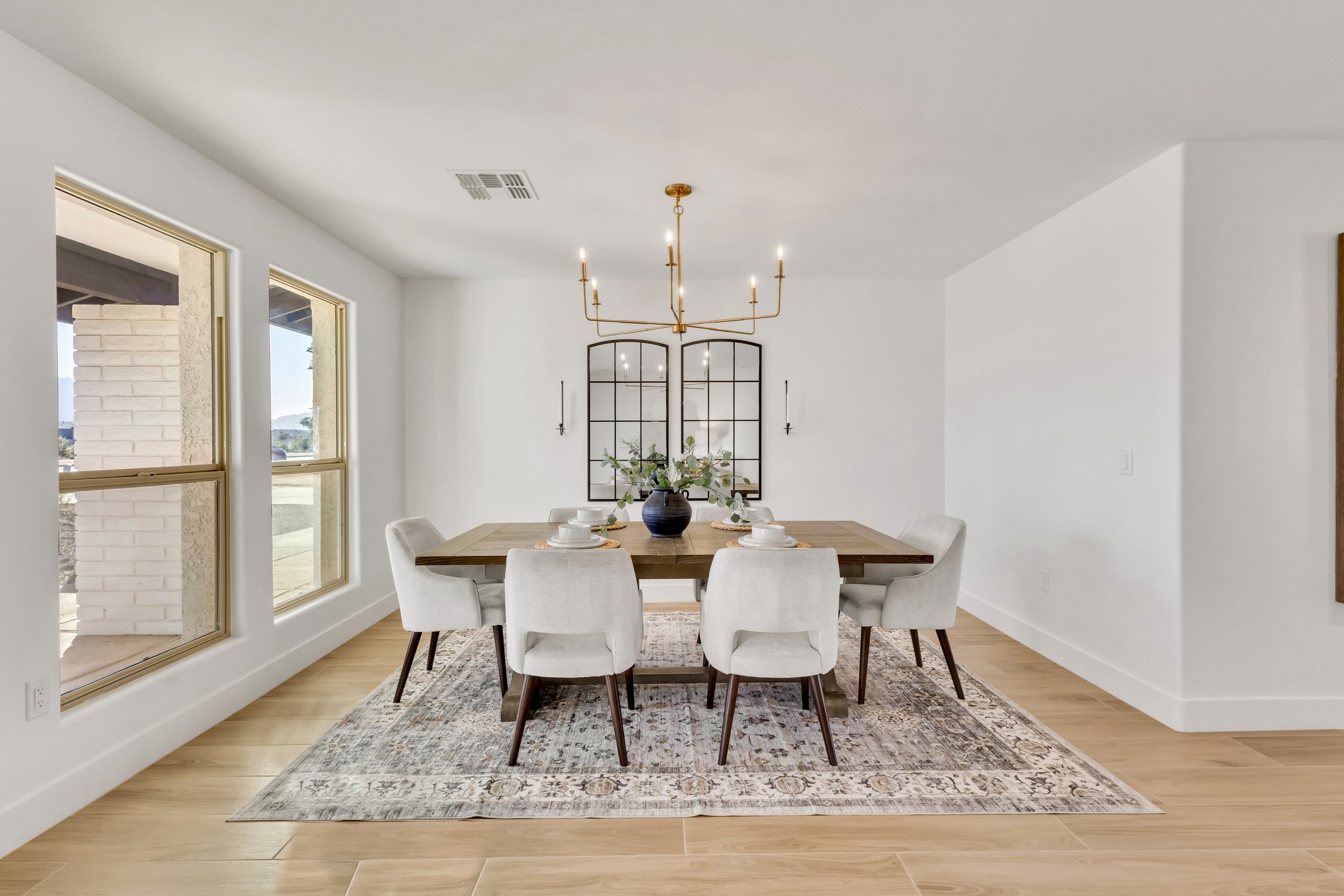 Bright dining room in Phoenix, AZ with a modern gold chandelier, wood table, and large windows providing natural light.