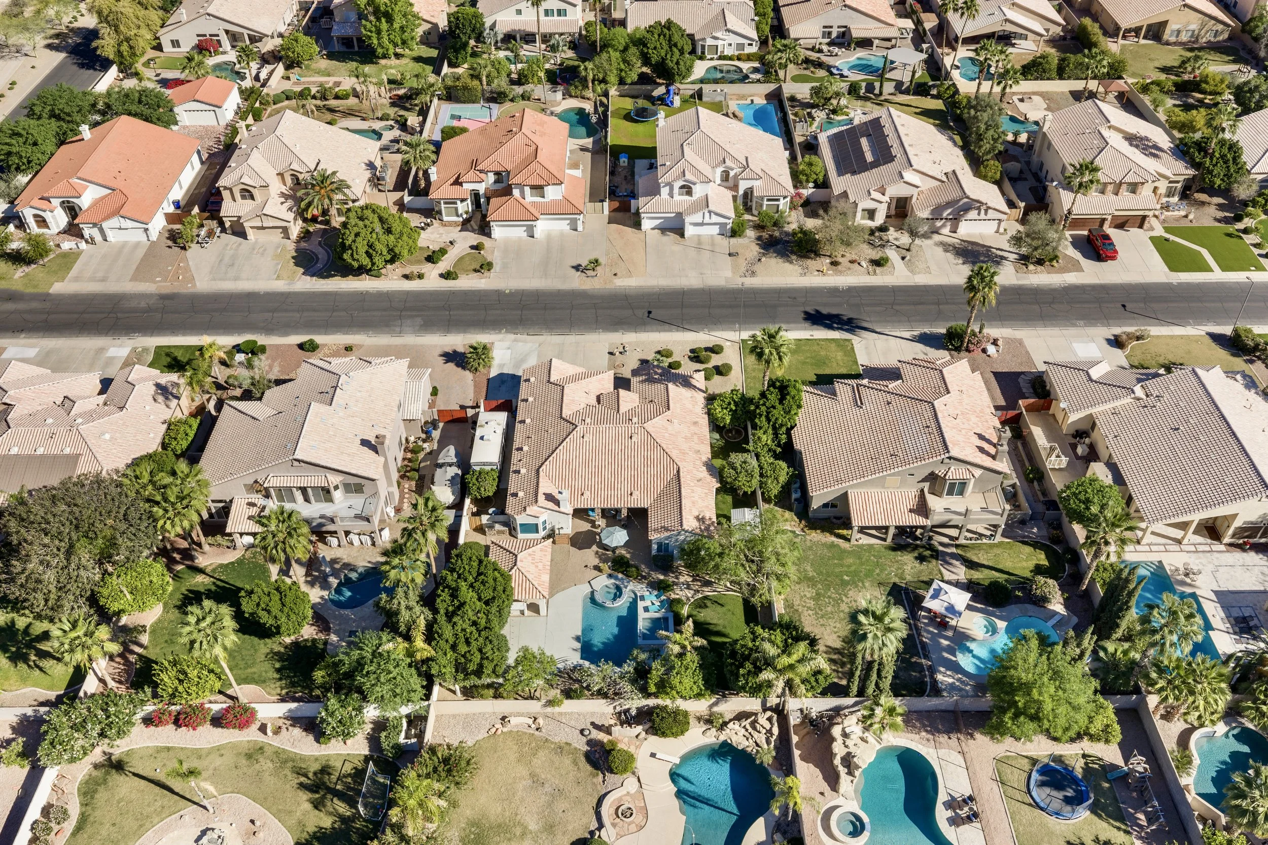 Aerial real estate photography of suburban homes with pools and green backyards in Gilbert, AZ, showcasing a beautiful and well-maintained neighborhood.