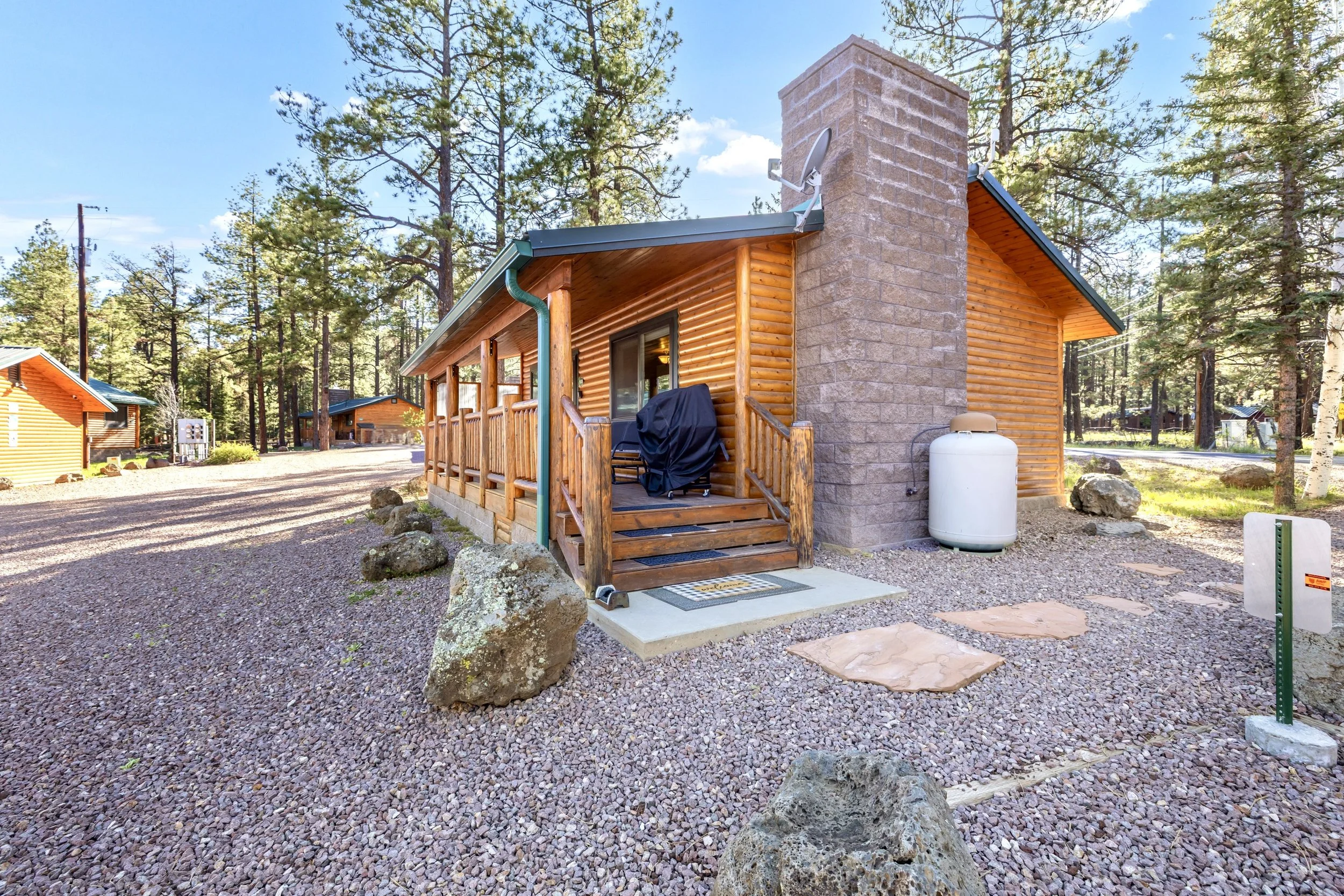 This log cabin exterior in Greer, AZ features a gravel yard surrounded by pine trees, captured with professional real estate photography showcasing its rustic charm and natural setting.