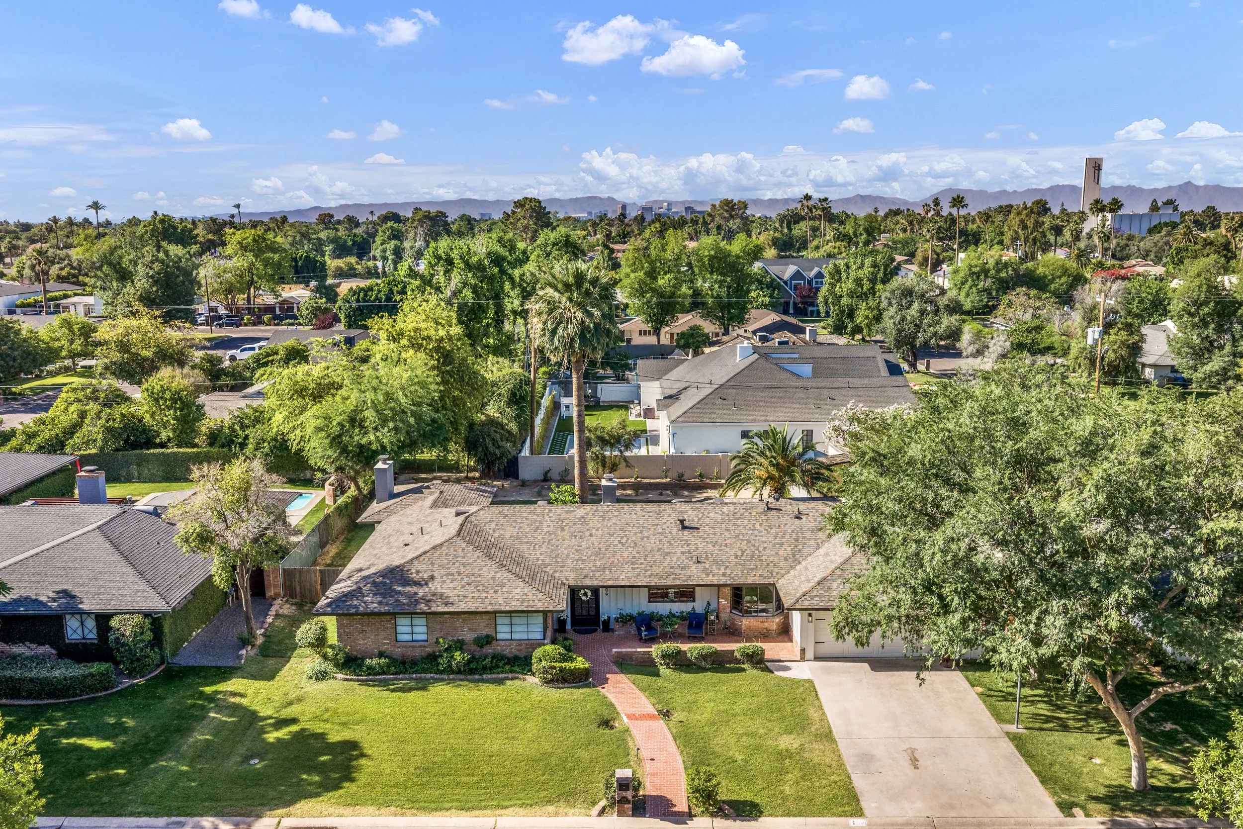 Aerial real estate photography of a suburban home with lush green landscaping and mountain views in Phoenix, AZ, showcasing a spacious front yard and clear skies.