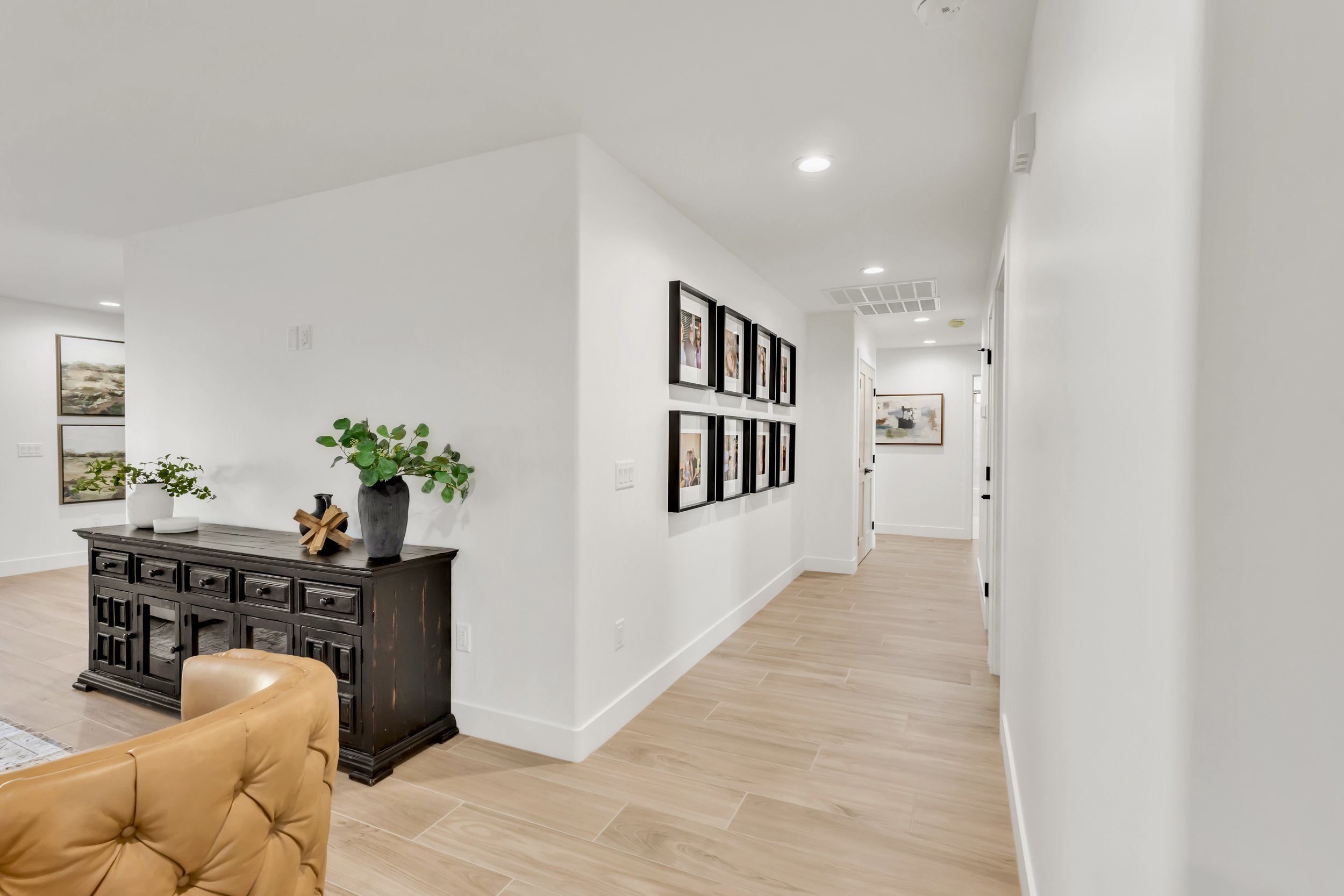 Interior hallway in Phoenix, AZ home featuring framed family photos, recessed lighting, and wood-look tile flooring.