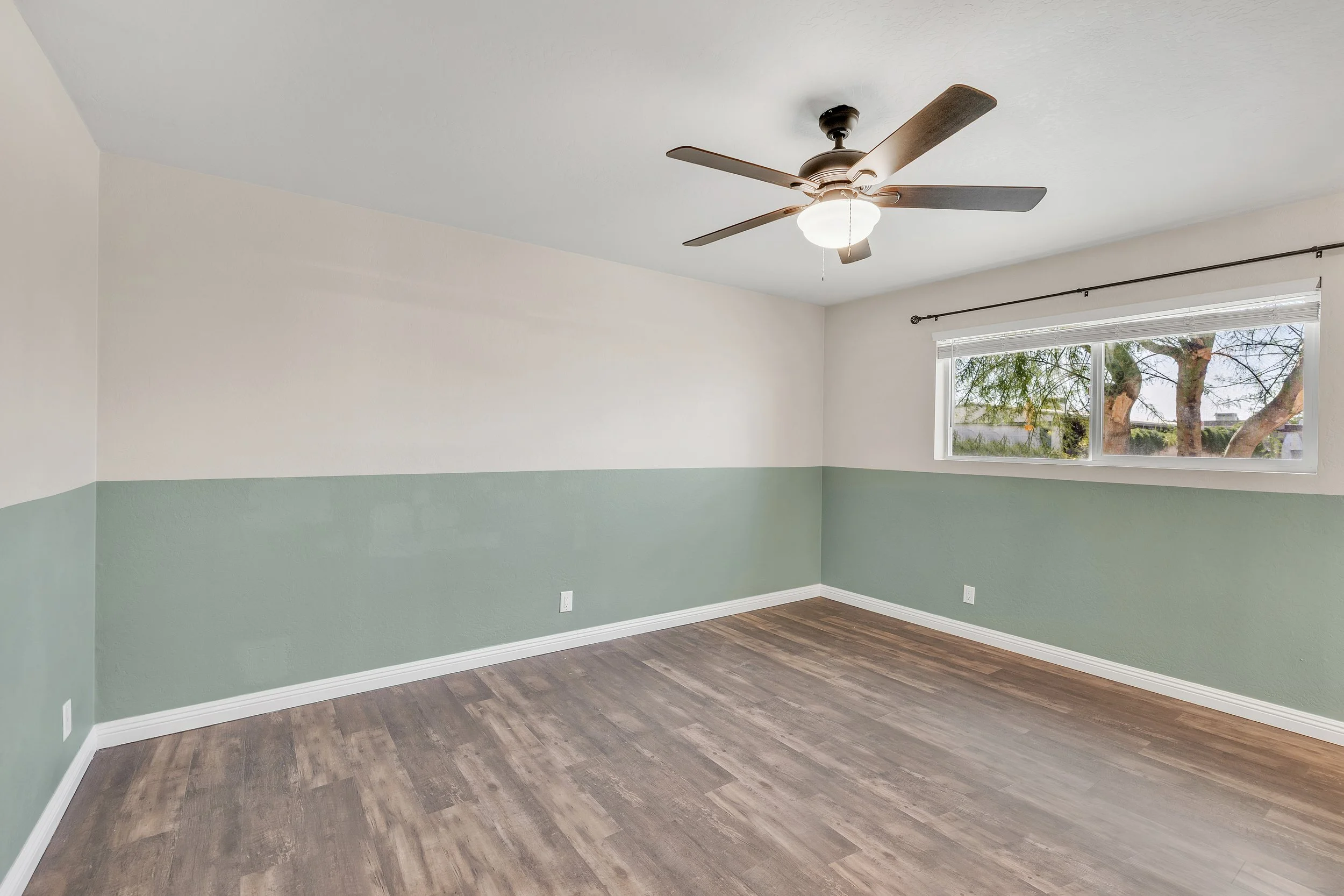 This vacant bedroom in Tempe, AZ features a ceiling fan, two-tone painted walls, and large windows, captured beautifully with professional real estate photography to highlight its spacious layout.