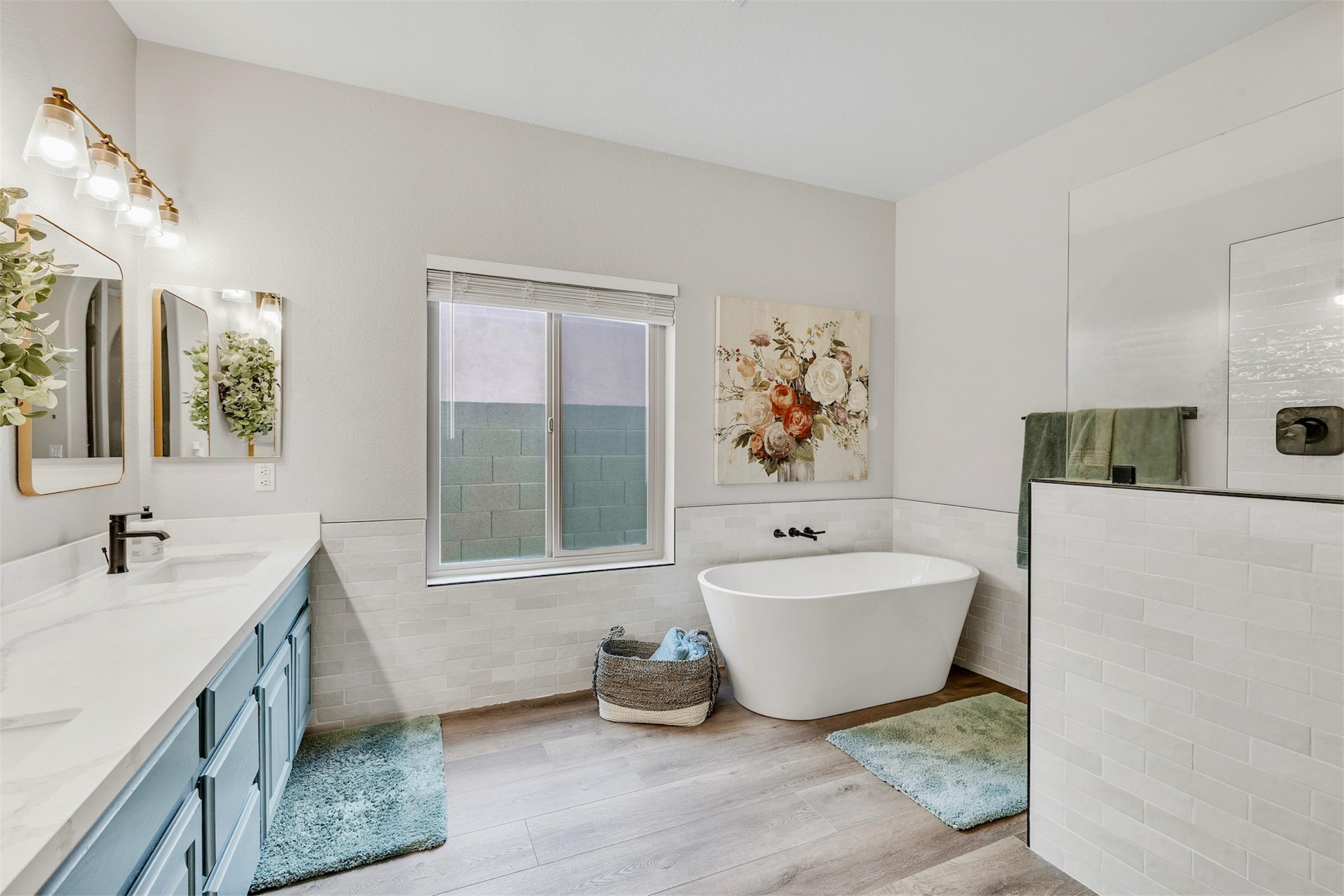 This modern bathroom in Goodyear, AZ features blue cabinets, a freestanding bathtub, and bright lighting, captured through professional real estate photography.