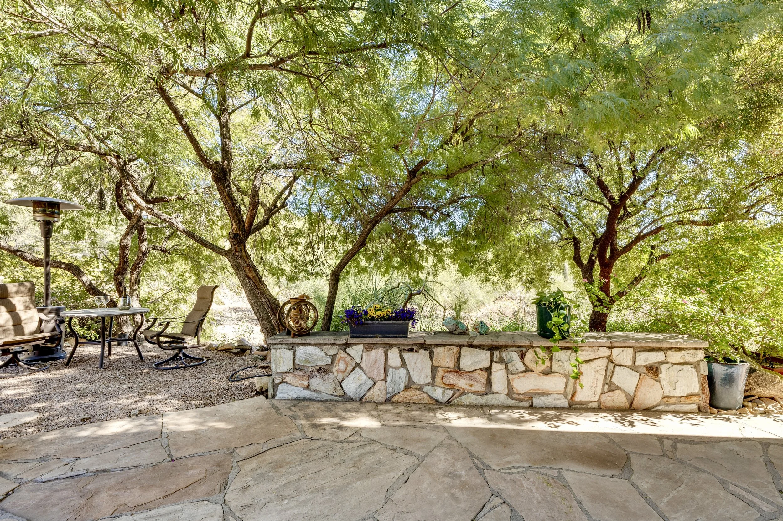 This shaded backyard patio in Paradise Valley, AZ features a stone wall and cozy seating area, showcasing beautiful real estate photography.