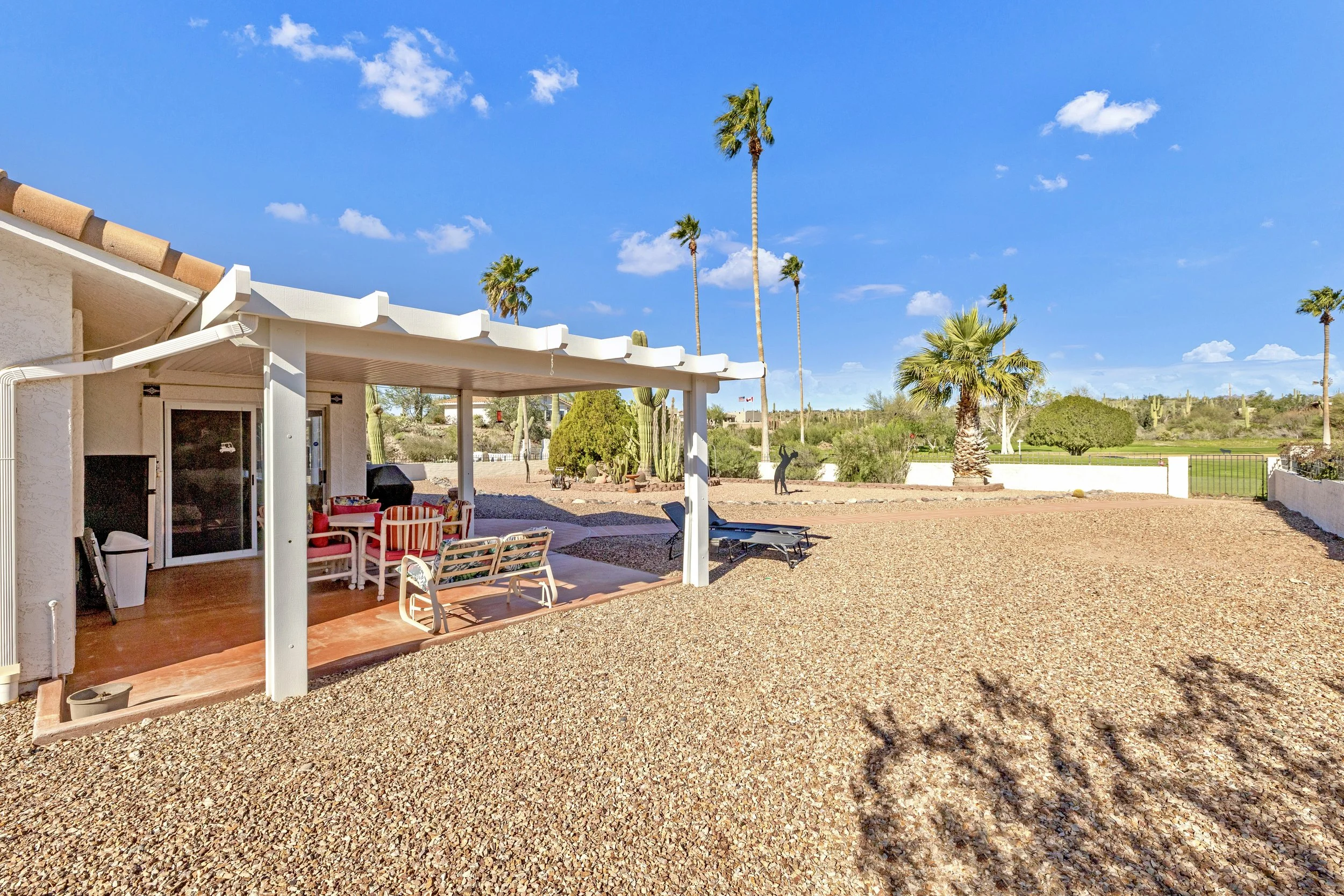 This real estate photography showcases a covered patio area and spacious pebble backyard in Queen Valley, AZ, highlighting outdoor living potential and desert landscaping.