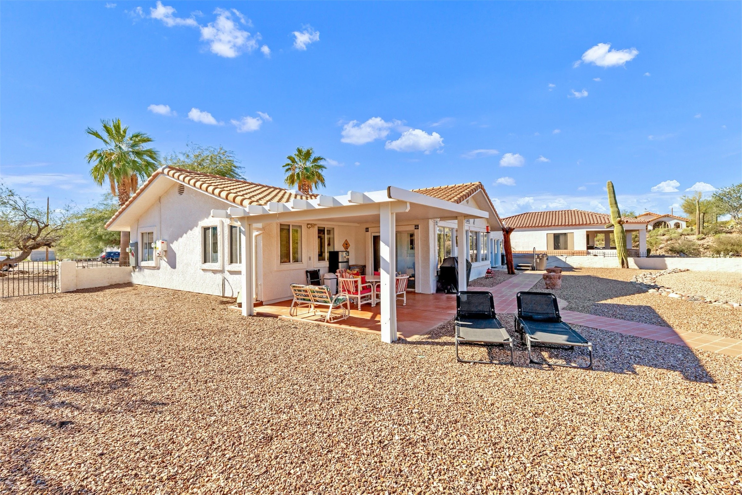 High-quality real estate photography showcases a charming Queen Valley, AZ home with patio seating and desert landscaping under a bright blue sky.