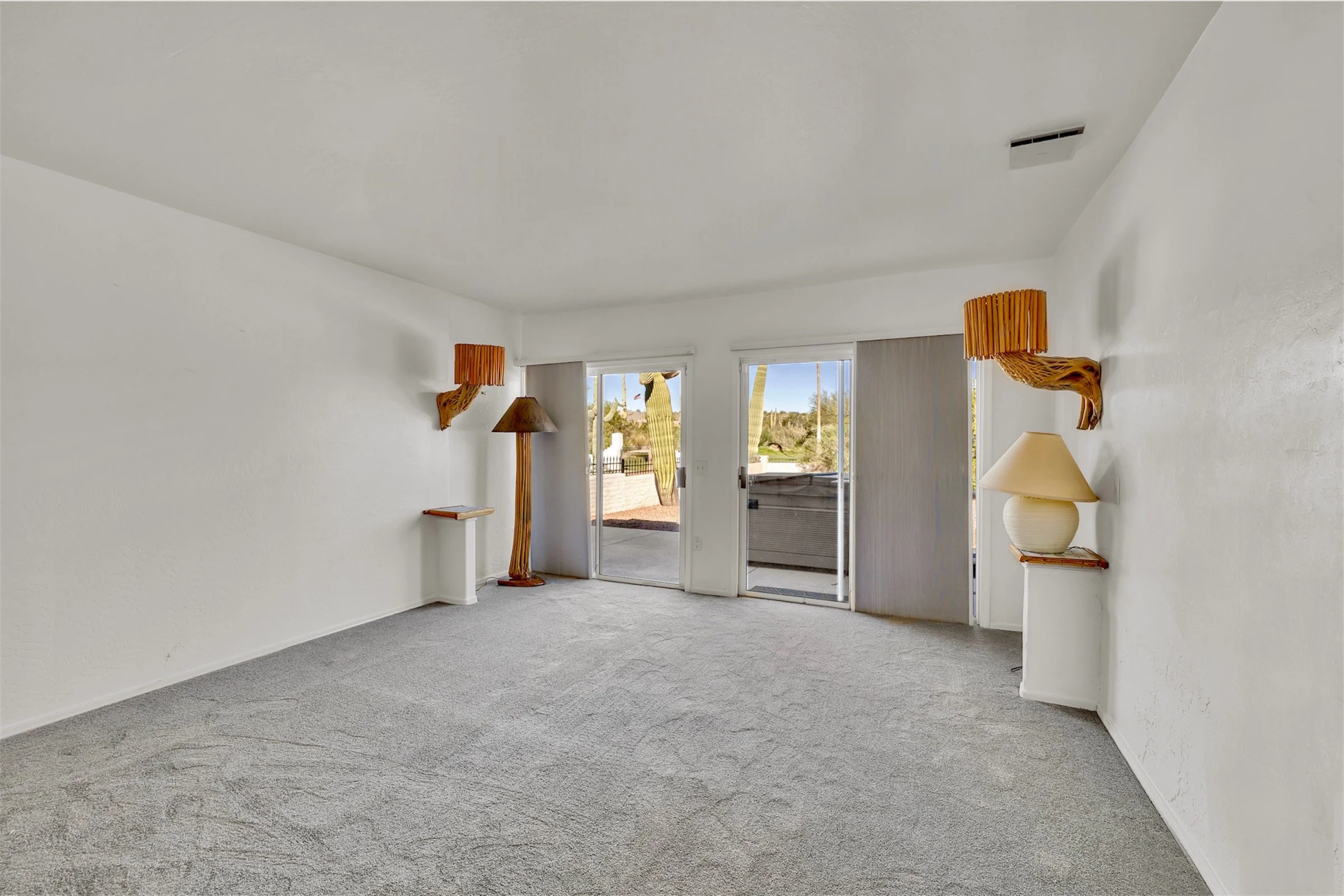 Bright empty living room with carpet flooring and sliding glass doors, showcased in real estate photography in Queen Valley, AZ, highlighting natural light and outdoor views.