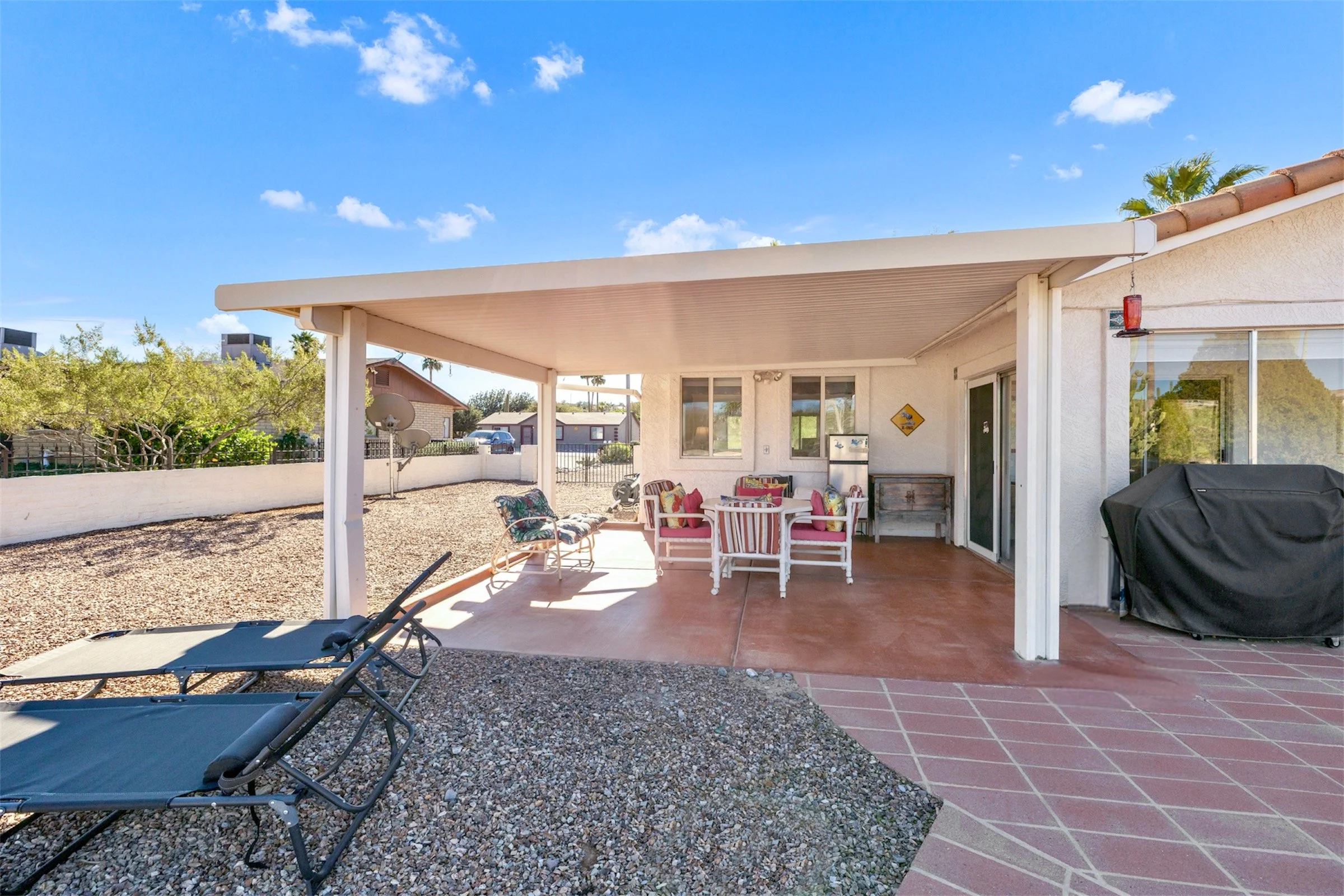 This photo showcases a covered patio with outdoor seating in Queen Valley, AZ, perfect for entertaining, captured with expert real estate photography to highlight the property's spacious backyard area.