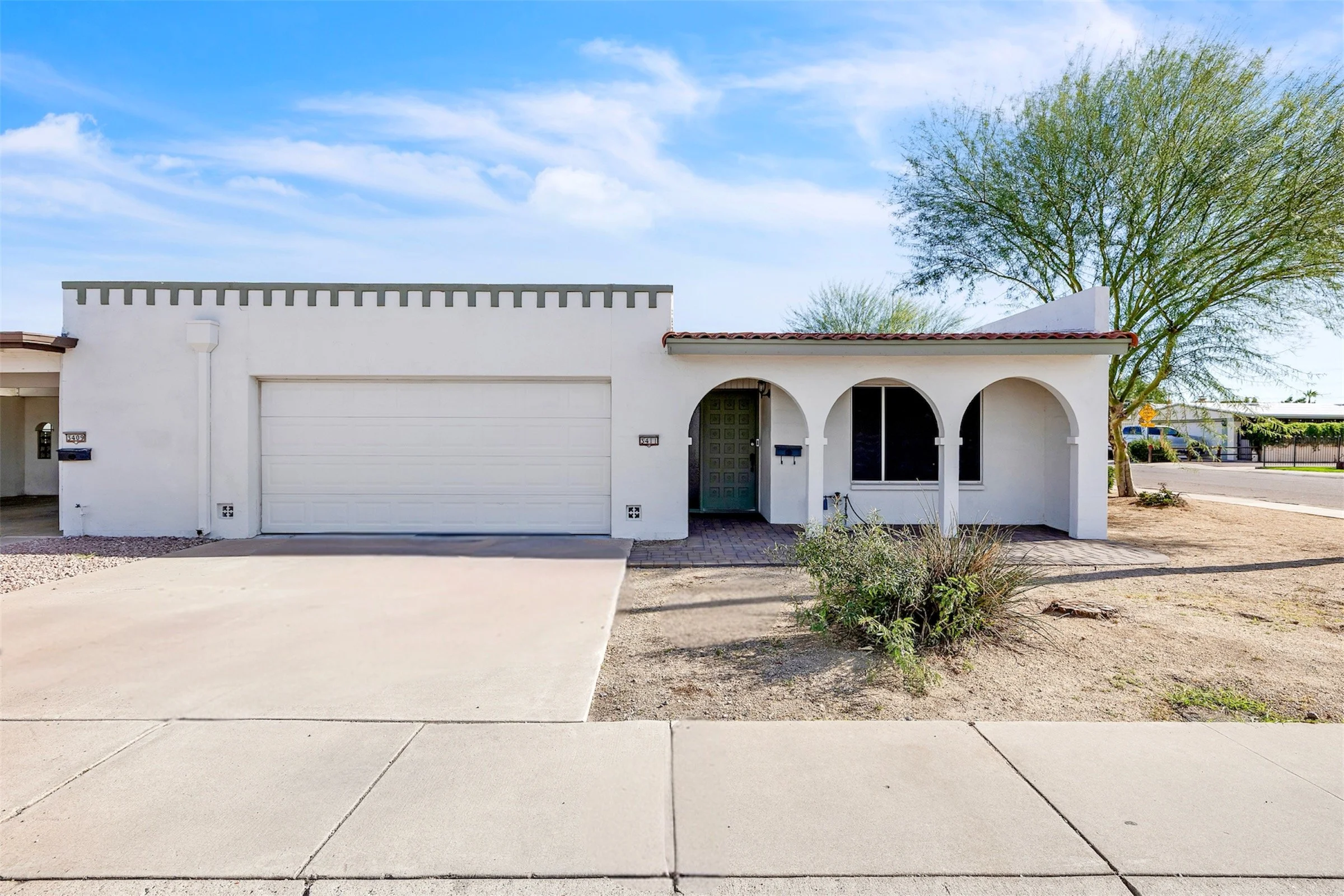 A white Spanish-style home with a two-car garage and arched front porch captured through professional real estate photography in Tempe, AZ.