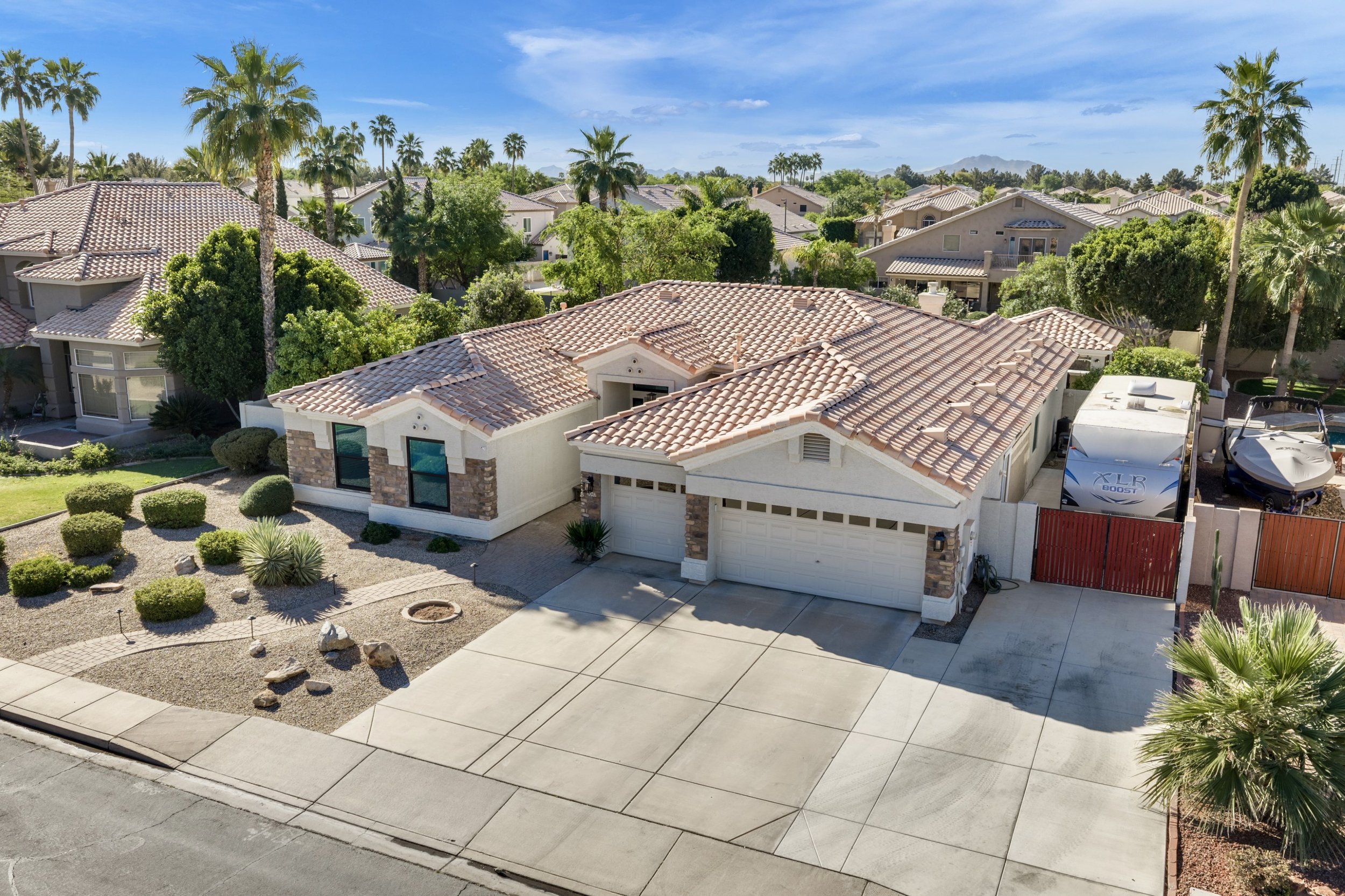 This aerial real estate photography showcases a suburban home with a tiled roof and spacious driveway in Gilbert, AZ, highlighting the well-maintained neighborhood with lush greenery and clear skies.
