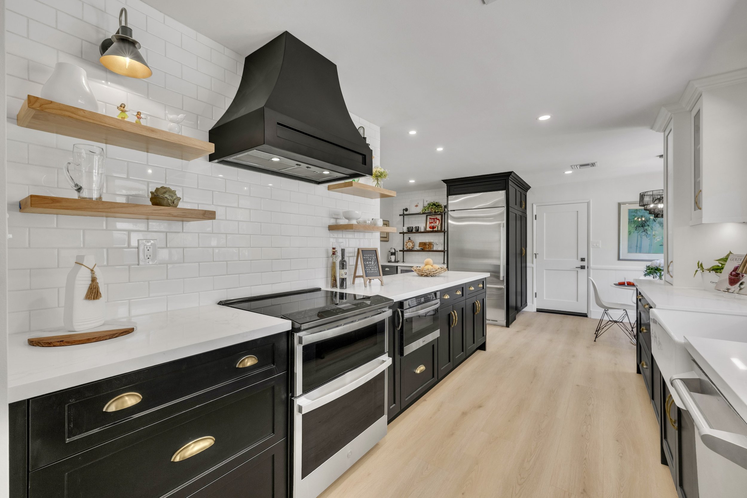 This modern kitchen in Phoenix, AZ features black cabinetry, stainless steel appliances, and light wood flooring, captured with expert real estate photography to highlight its stylish design and spacious layout.