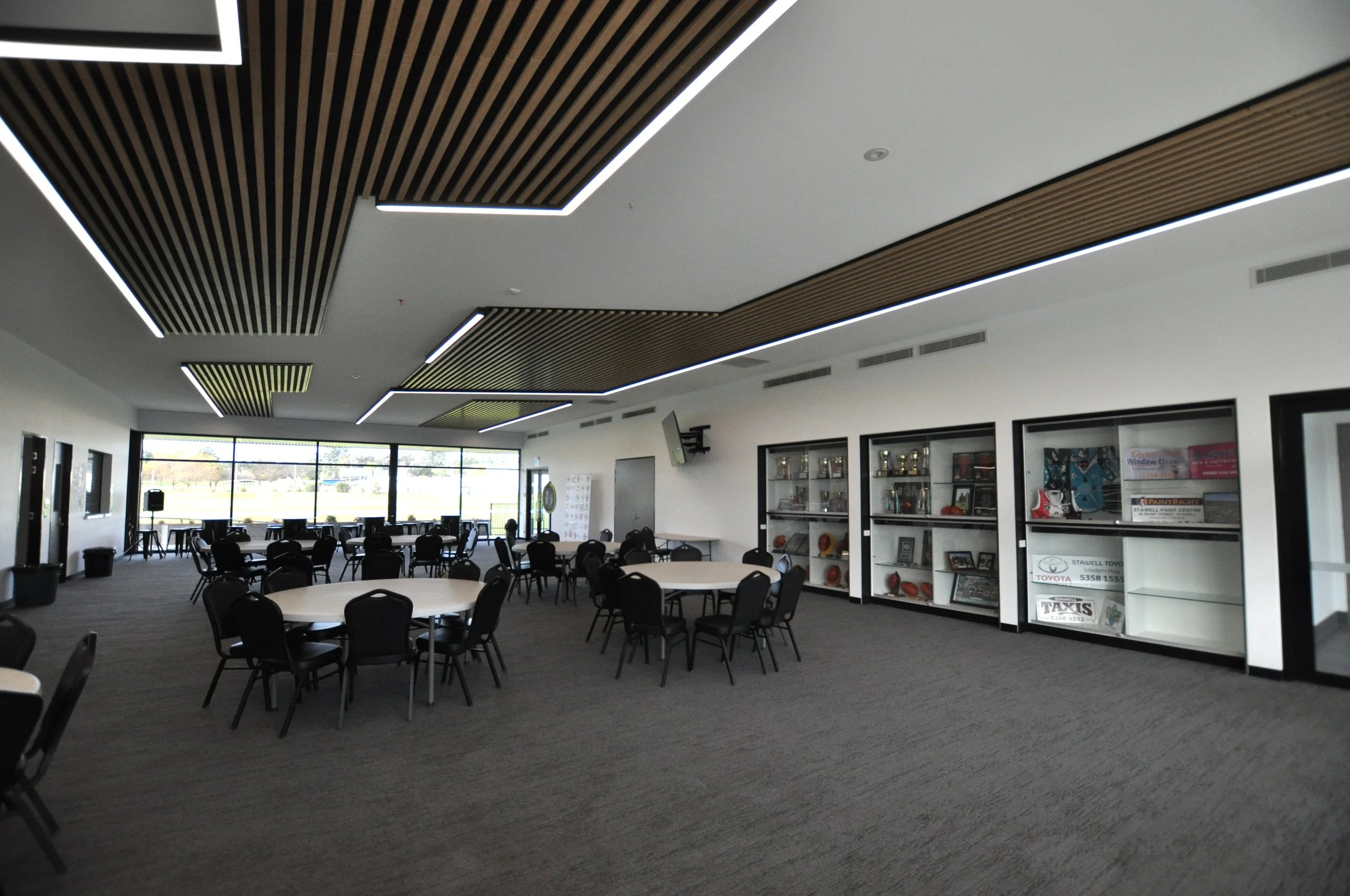 A spacious room with round tables, black chairs, large windows, and display cases with trophies and memorabilia.