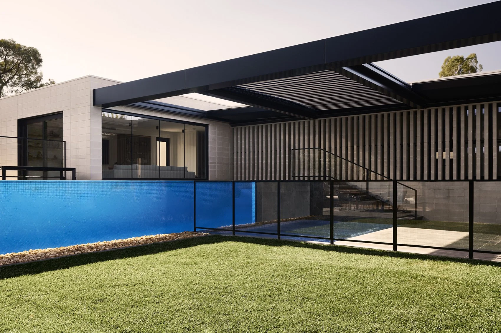 Modern house with large windows, outdoor pool, and a grassy lawn, featuring a black metal fence and wooden accents.