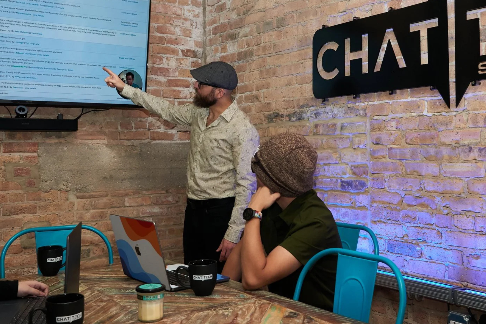 Candid shot of Burak Sarac and Chat Tech team having a meeting at the conference room with brick walls and drinking coffee.