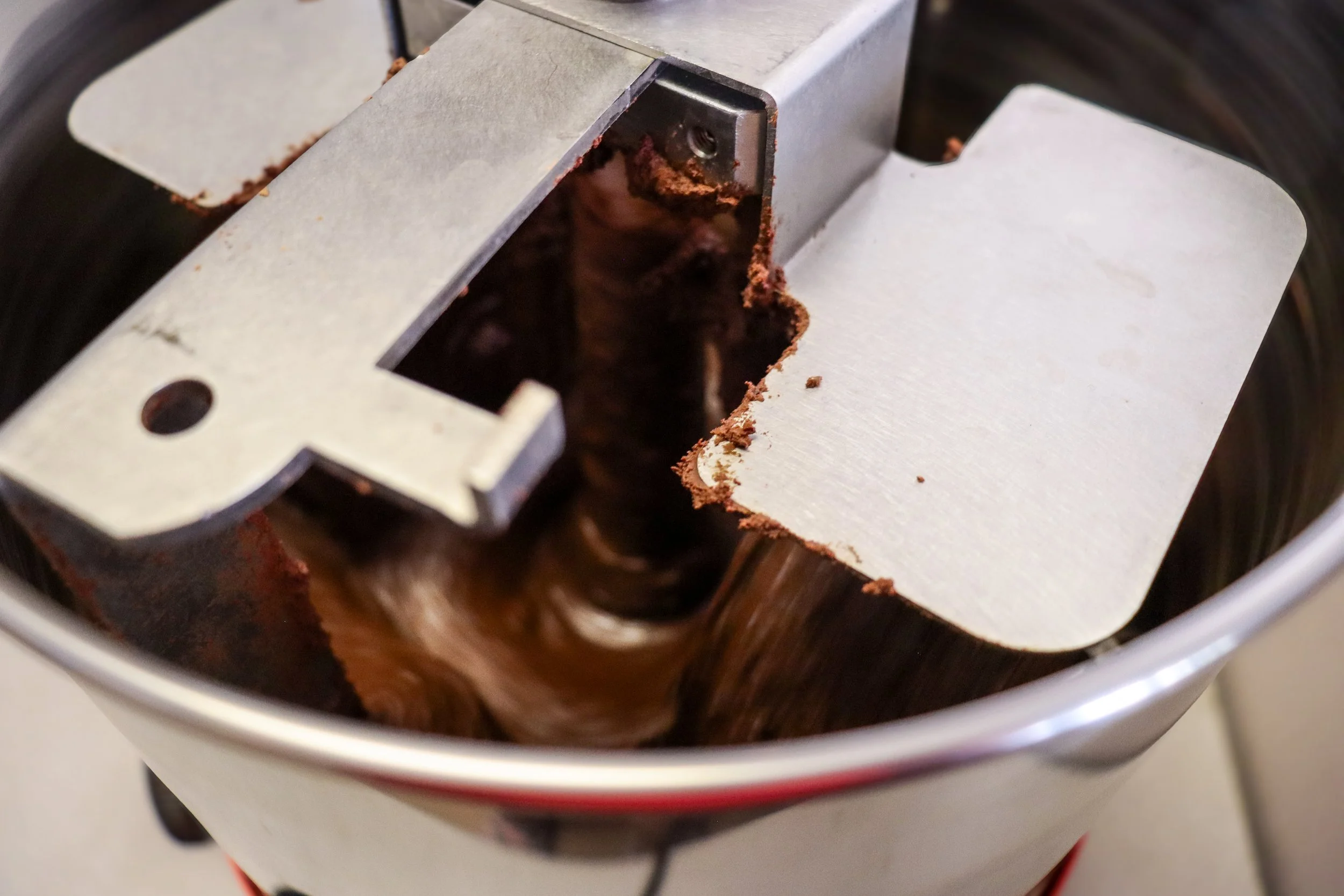 Close-up of a stone grinder melanger with a partially removed cover, showing ground chocolate inside.