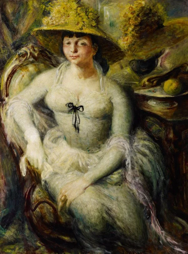 A woman sitting in a chair, wearing a wide-brimmed hat decorated with foliage. She has a relaxed expression, wearing a light-colored dress with a black ribbon, with a full background of greenery and flowers.