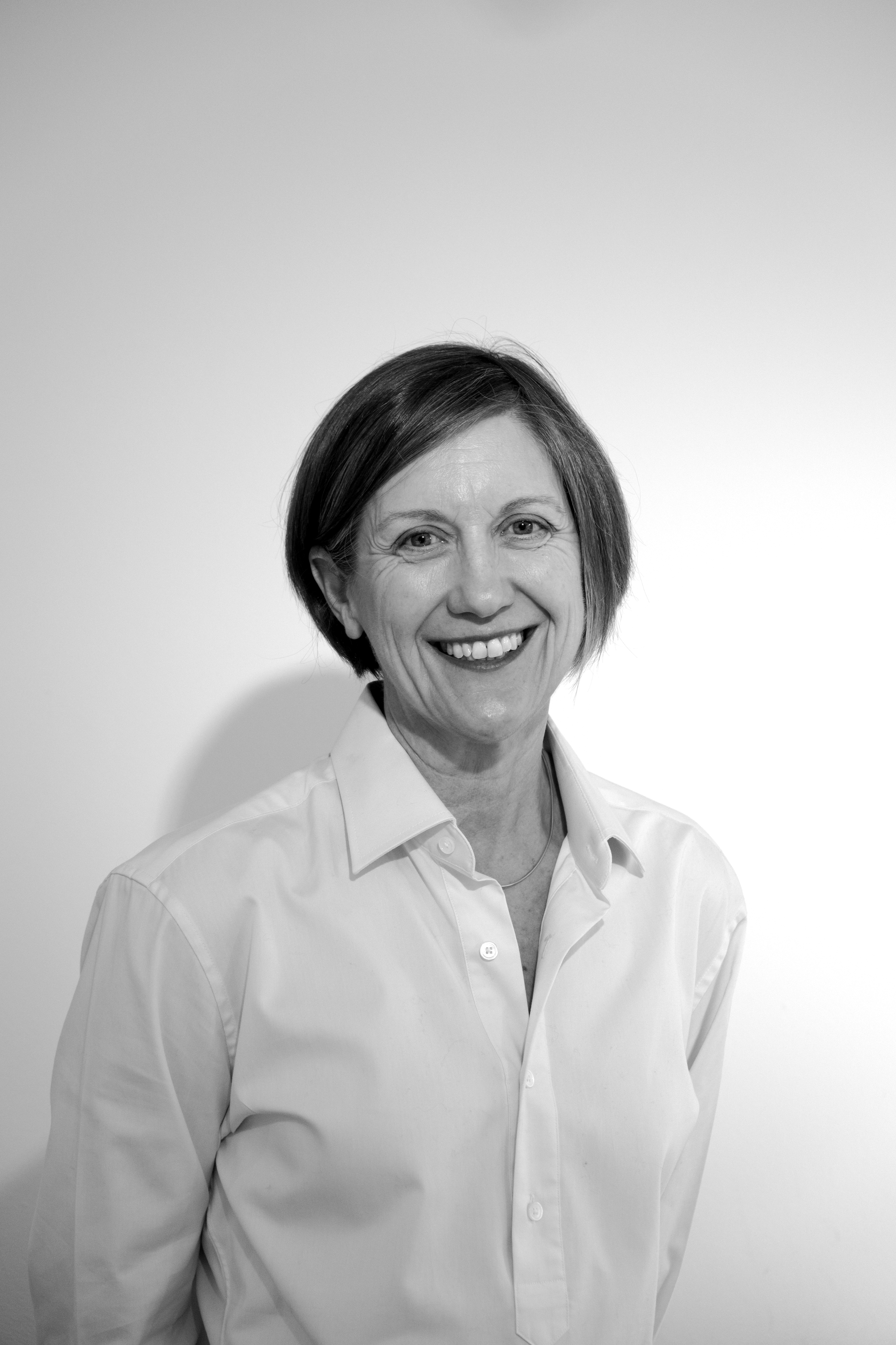 Black and white photo of a woman smiling, wearing a collared shirt, standing against a plain light background.