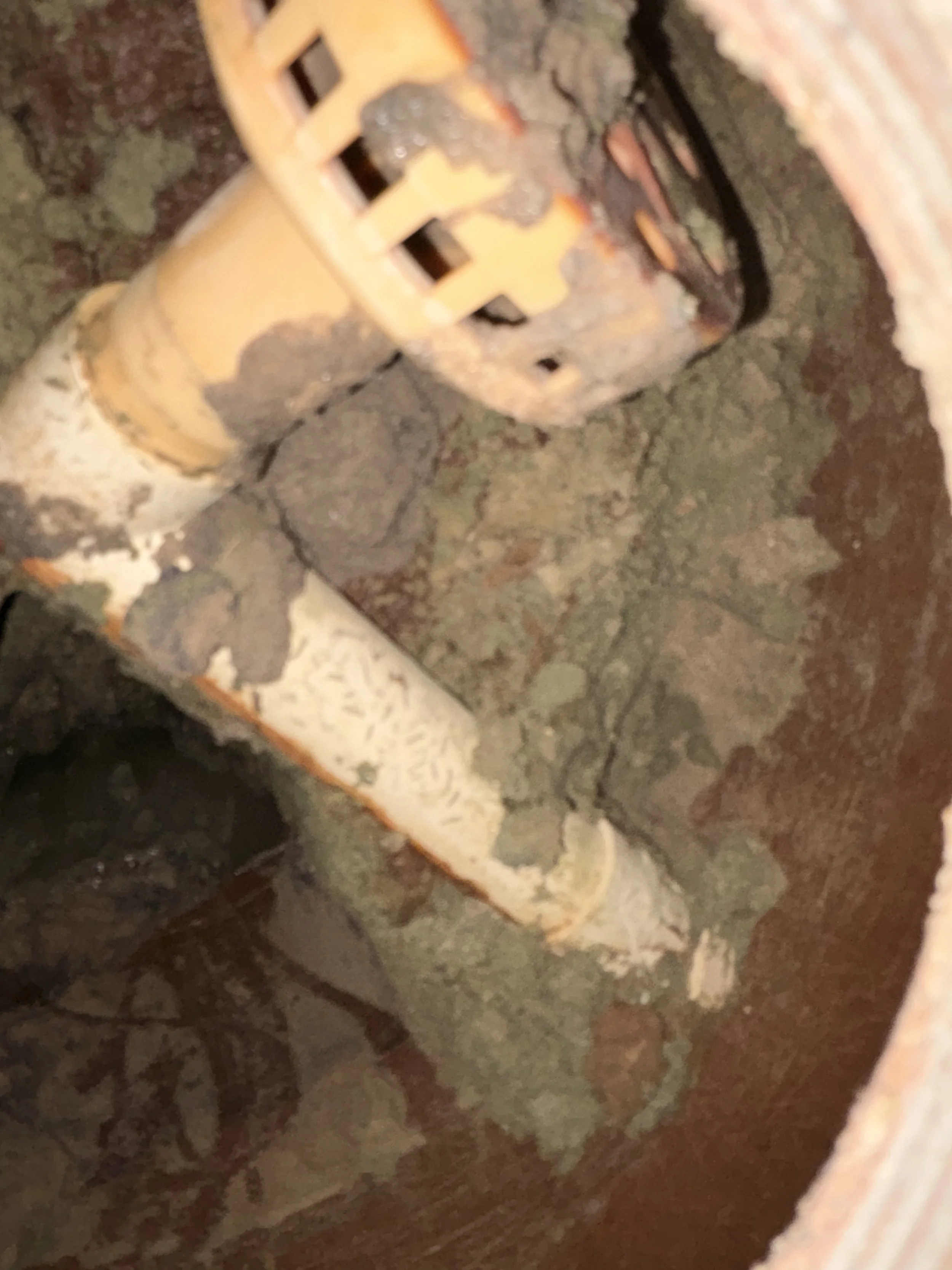 Close-up image of a rusty metal pipe with a valve and a grate, showing signs of corrosion and dirt.
