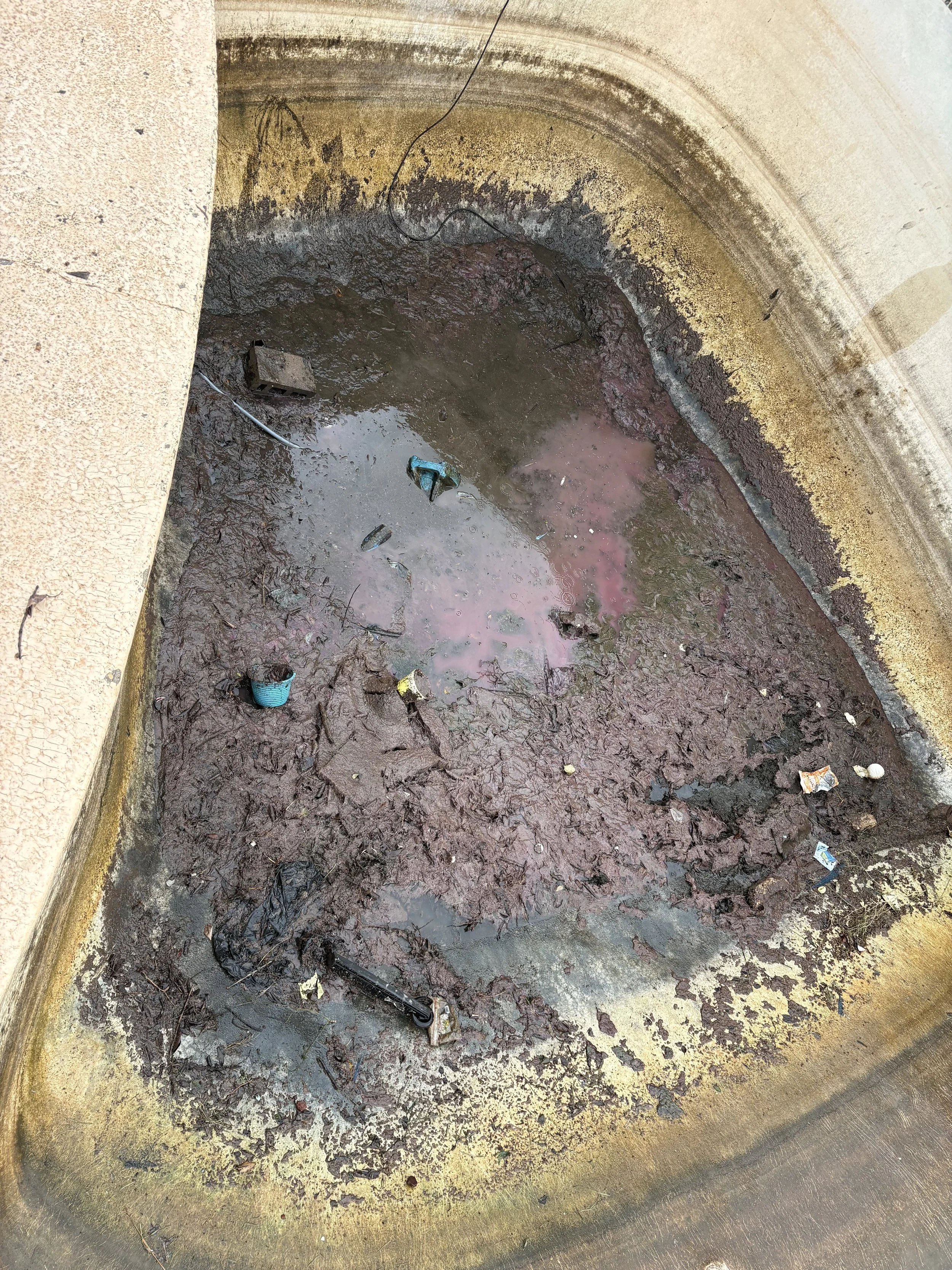 A dirty, water-filled, and trash-filled metal sink or basin with grime and debris around the edges and inside.