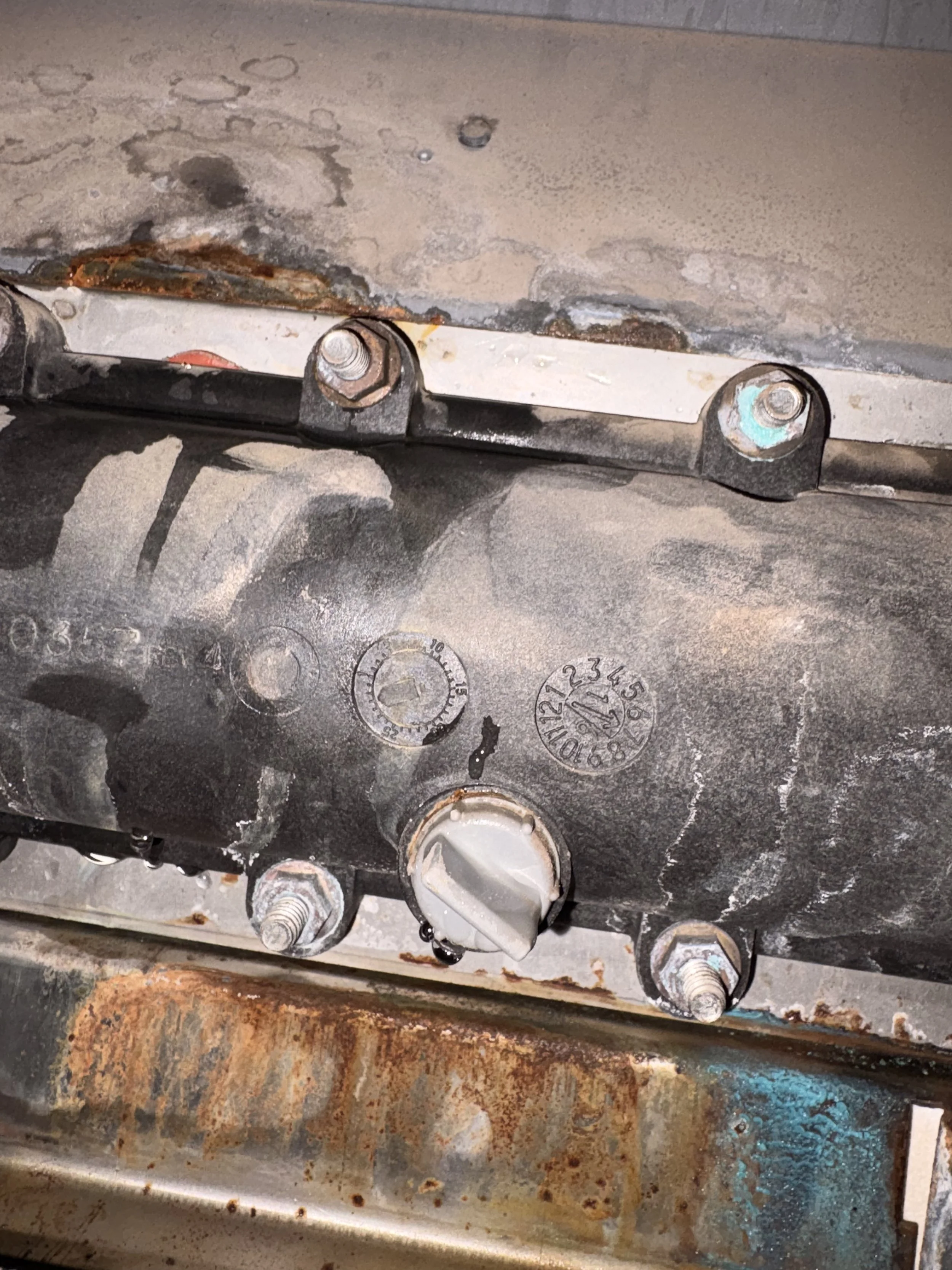 Close-up of a rusty, greasy mechanical component with various bolts and markings, showing signs of corrosion and dirt.