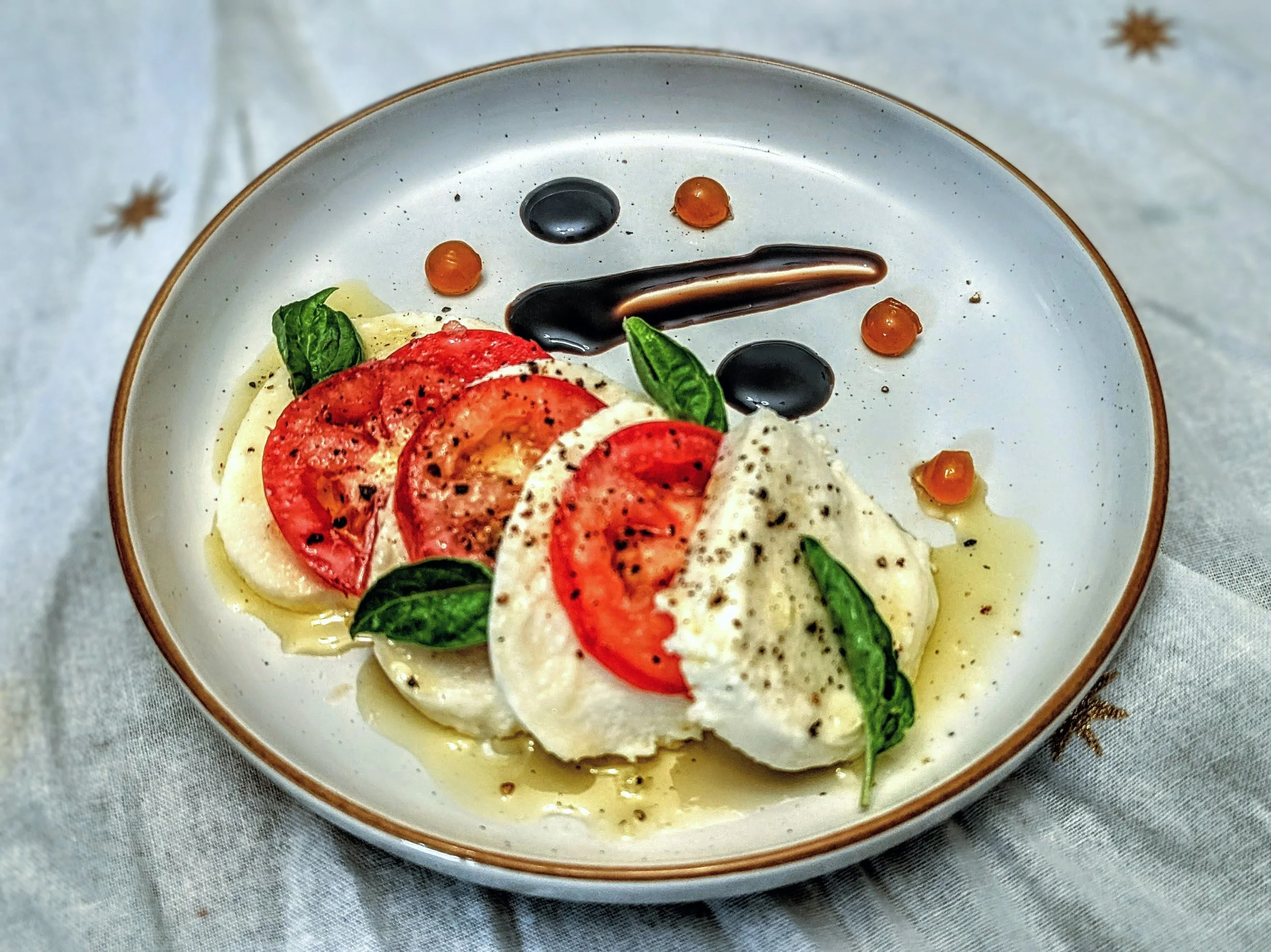 Caprese salad layered with fresh mozzarella and ripe Roma tomatoes, dressed with extra virgin olive oil, balsamic glaze, Maldon salt, cracked pepper, and finished with hot honey pearls for a private dining experience in Tucson, Arizona