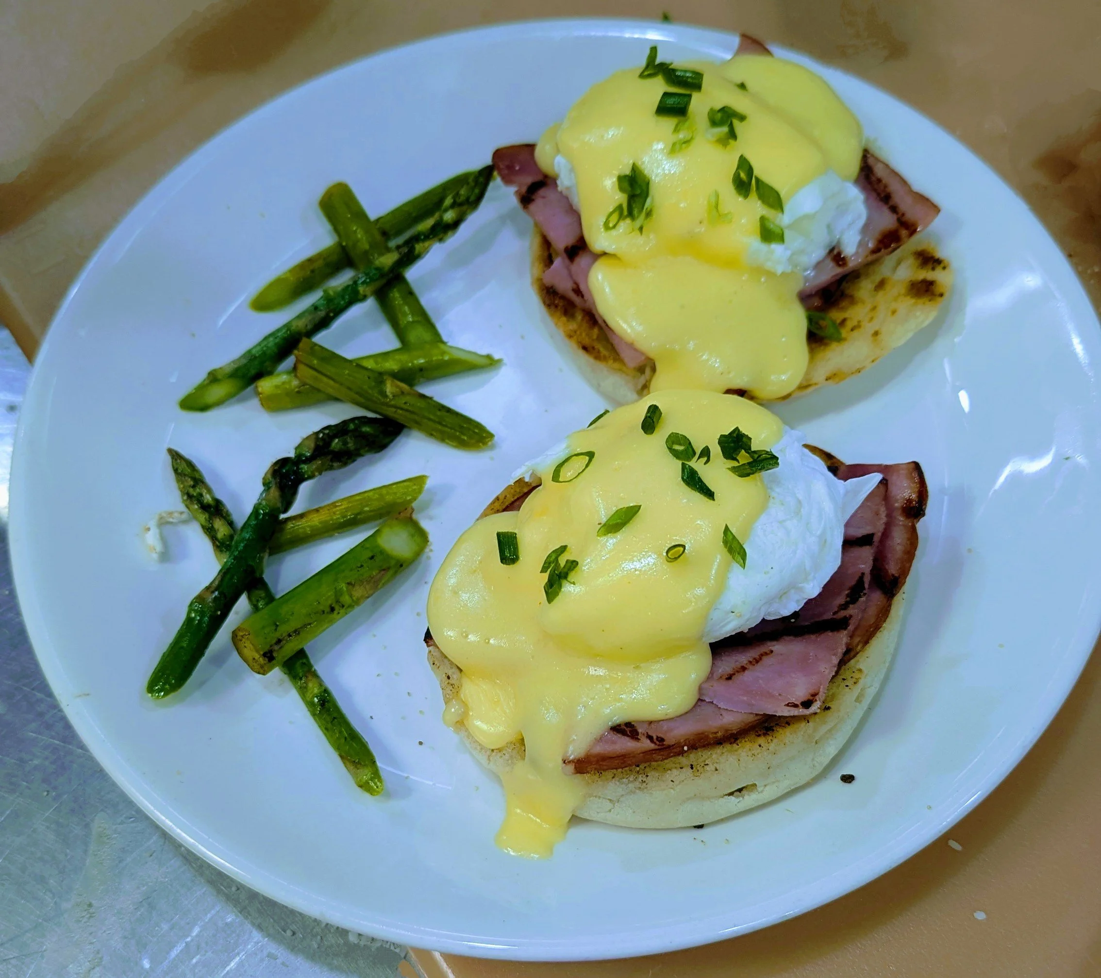 Eggs Benedict. Two poached eggs, over Canadian bacon and toasted English muffin with a rich classic hollandaise sauce, served with grilled asparagus on a white plate.