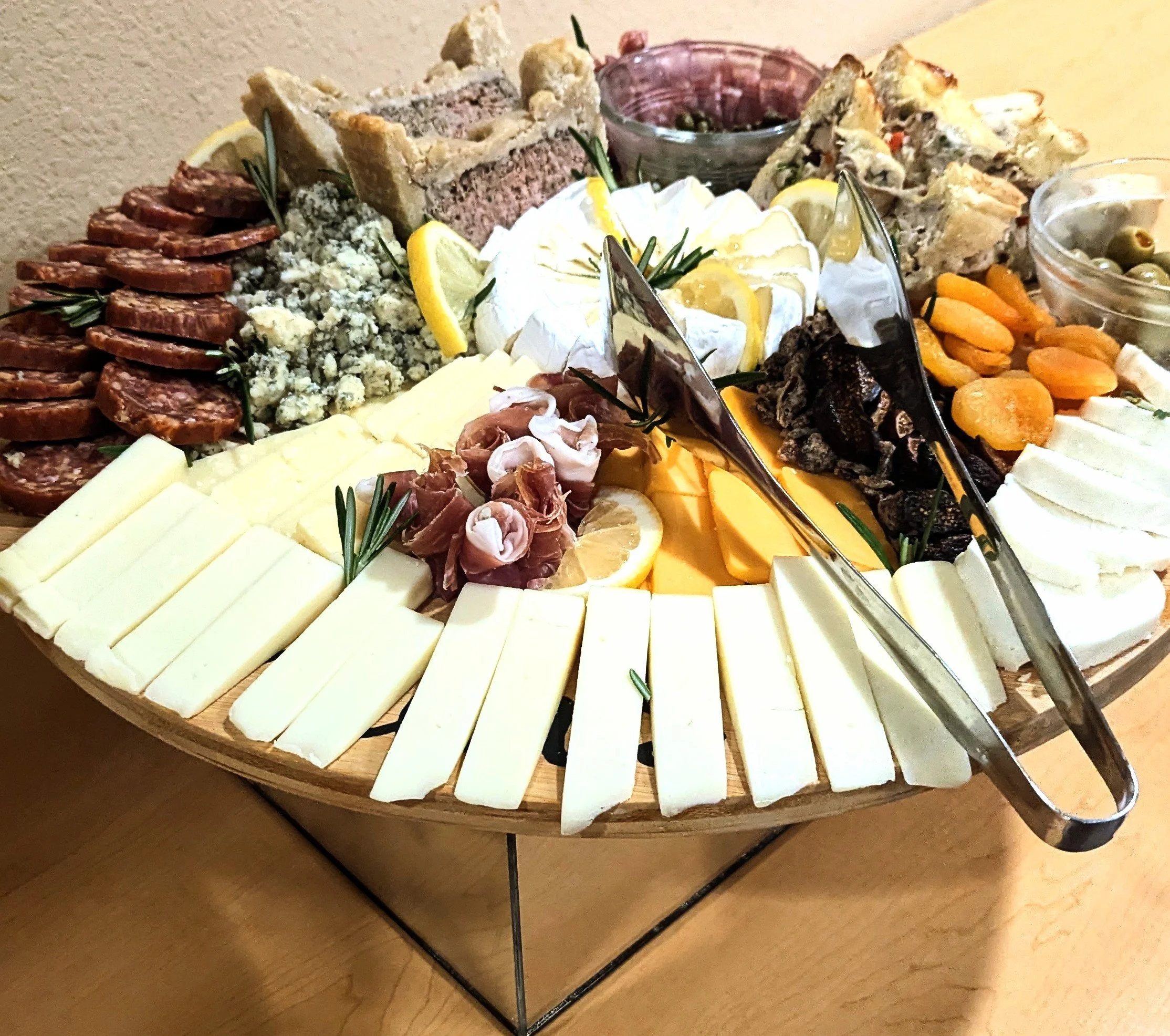 Charcuterie board with various cheeses, cured meats, nuts, crackers, and fruit garnishes.