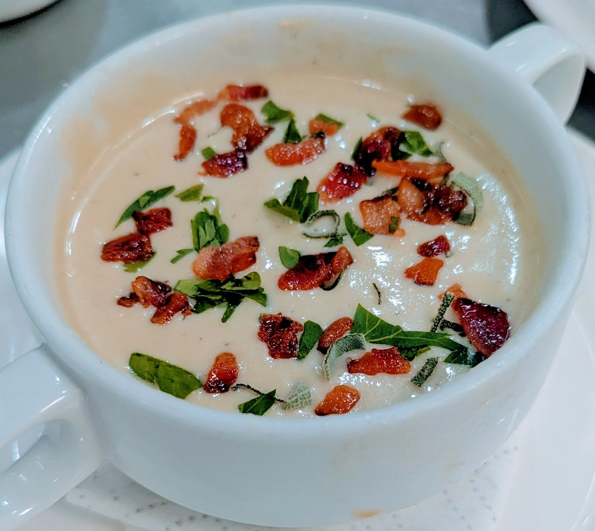 potato and leak soup, vichyssoise in a white mug topped with fried prosciutto, and chopped parsley.