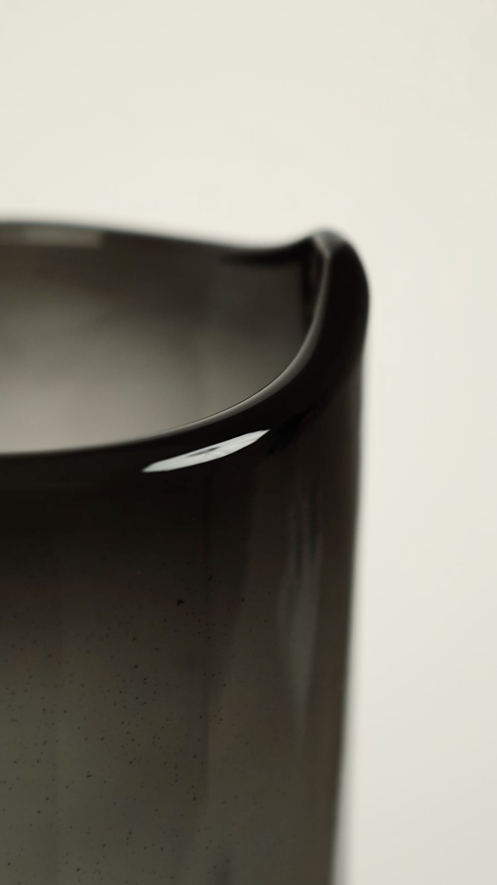 Close-up of the rim and side of a black ceramic mug on a light background.