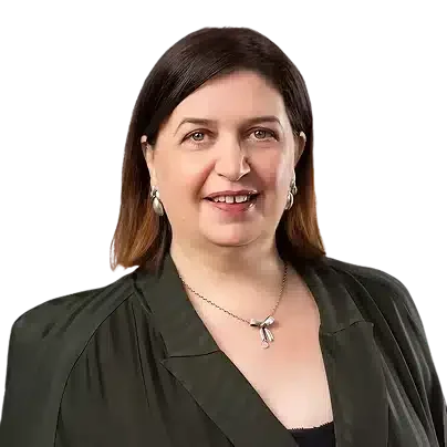 A woman with dark brown hair, wearing a black blazer and silver jewelry, smiling against a black background.
